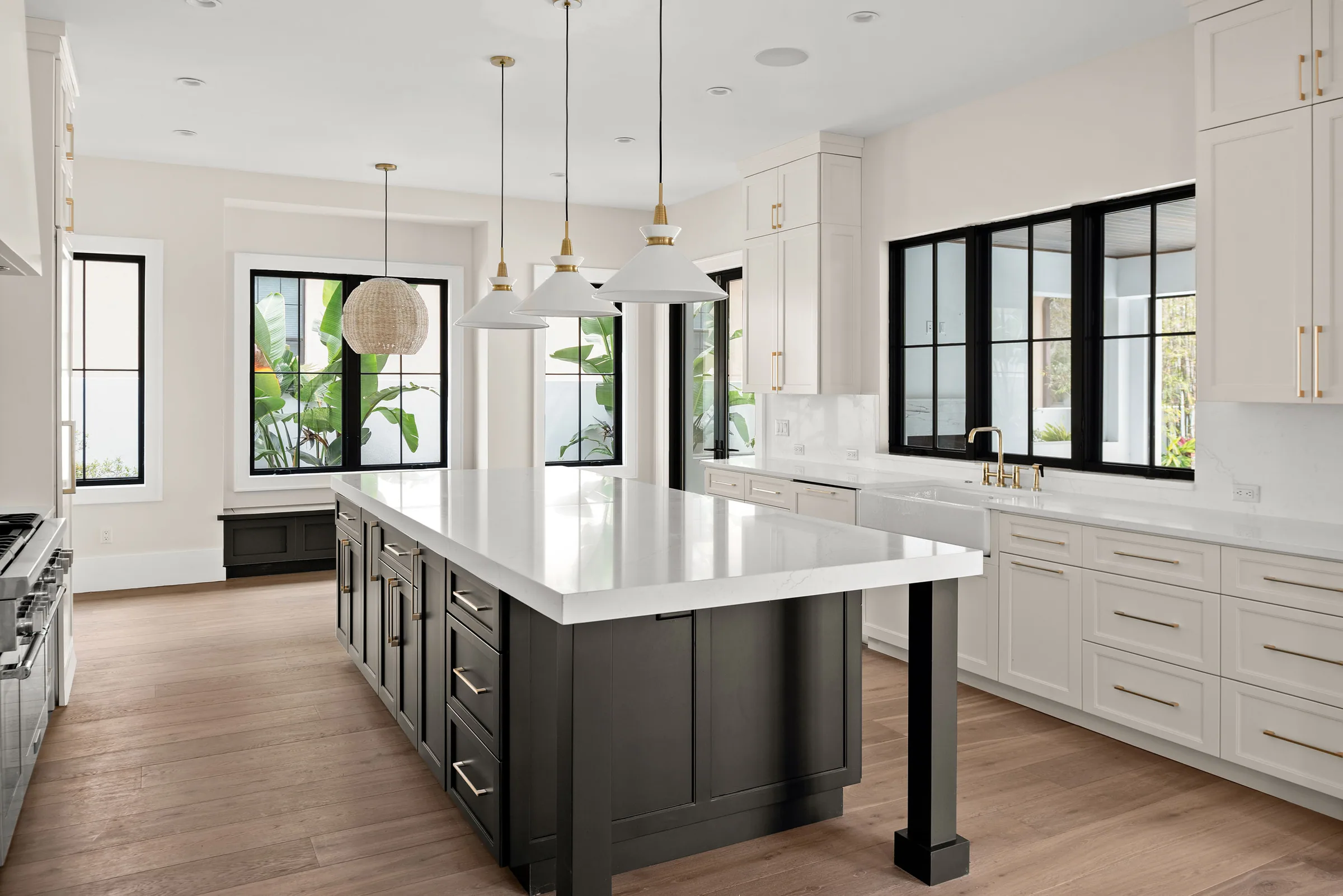 Kitchen with a charcoal island, white cabinets, three pendant lights and an apron-front sink below black-framed windows.