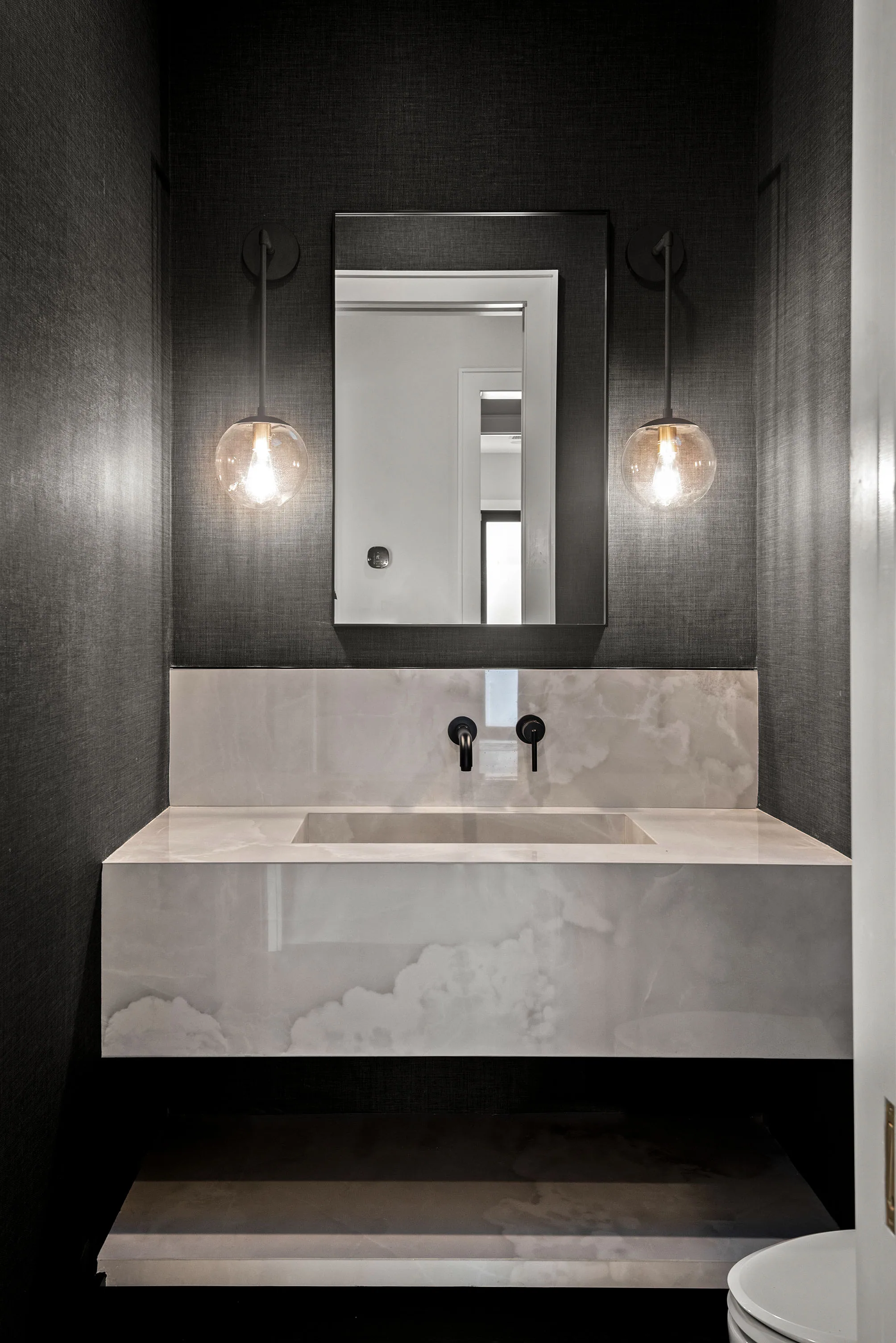 Dark powder room with a pale floating basin, black wall-mounted faucet and two glass globe sconces.