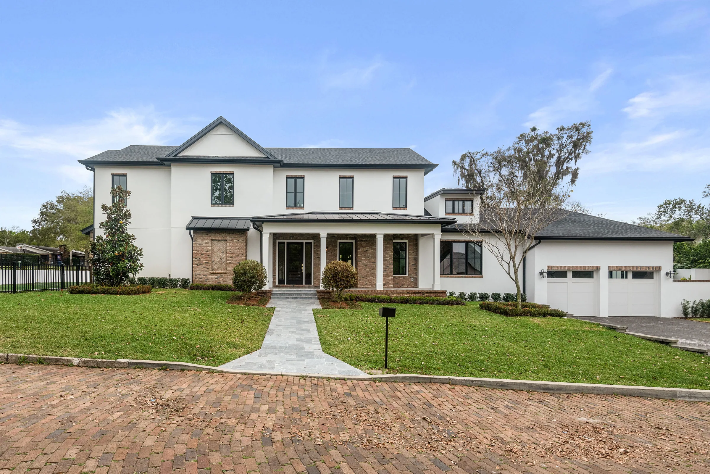 Restored two-story residence with a brick-accented front porch, white walls, dark-framed windows and garage.