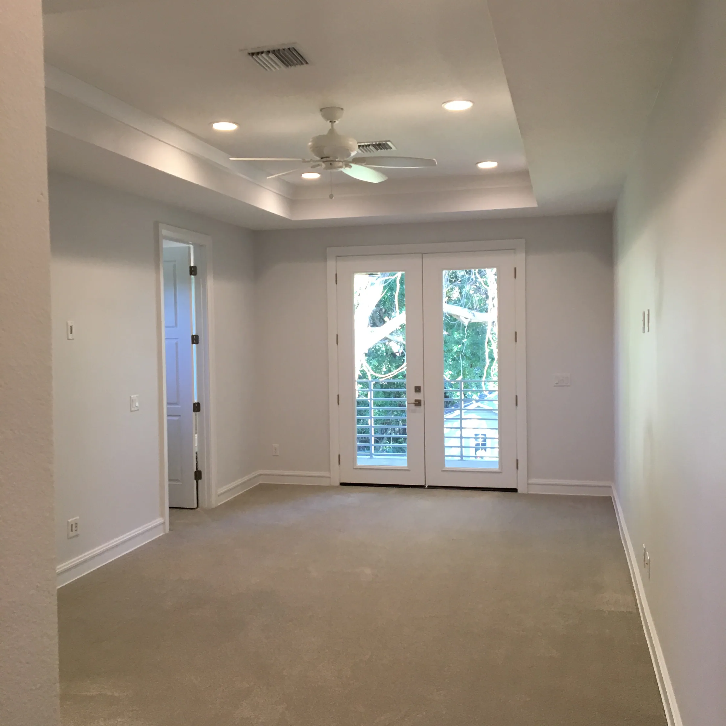 Carpeted bedroom with a tray ceiling, ceiling fan and glazed double doors to a balcony.