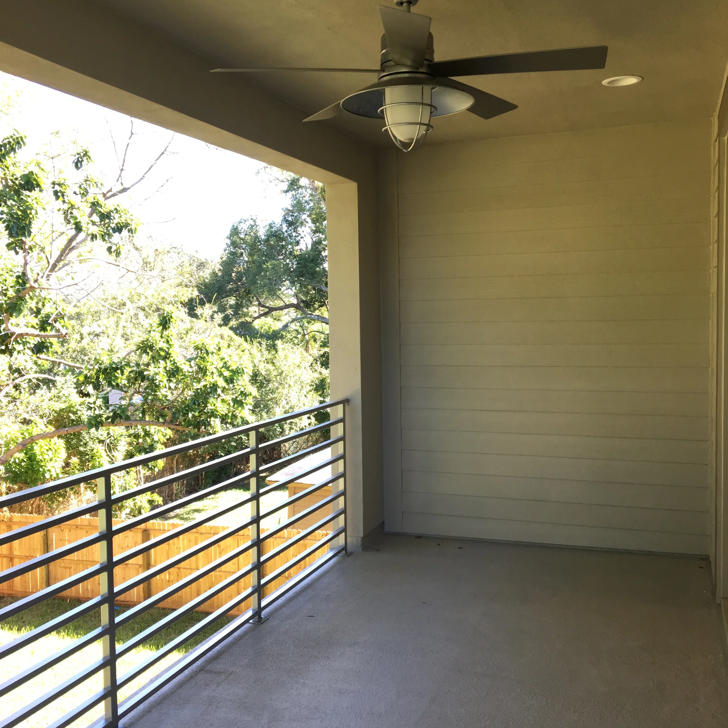 Covered East Evans balcony with a ceiling fan, horizontal metal railings and views of mature trees.