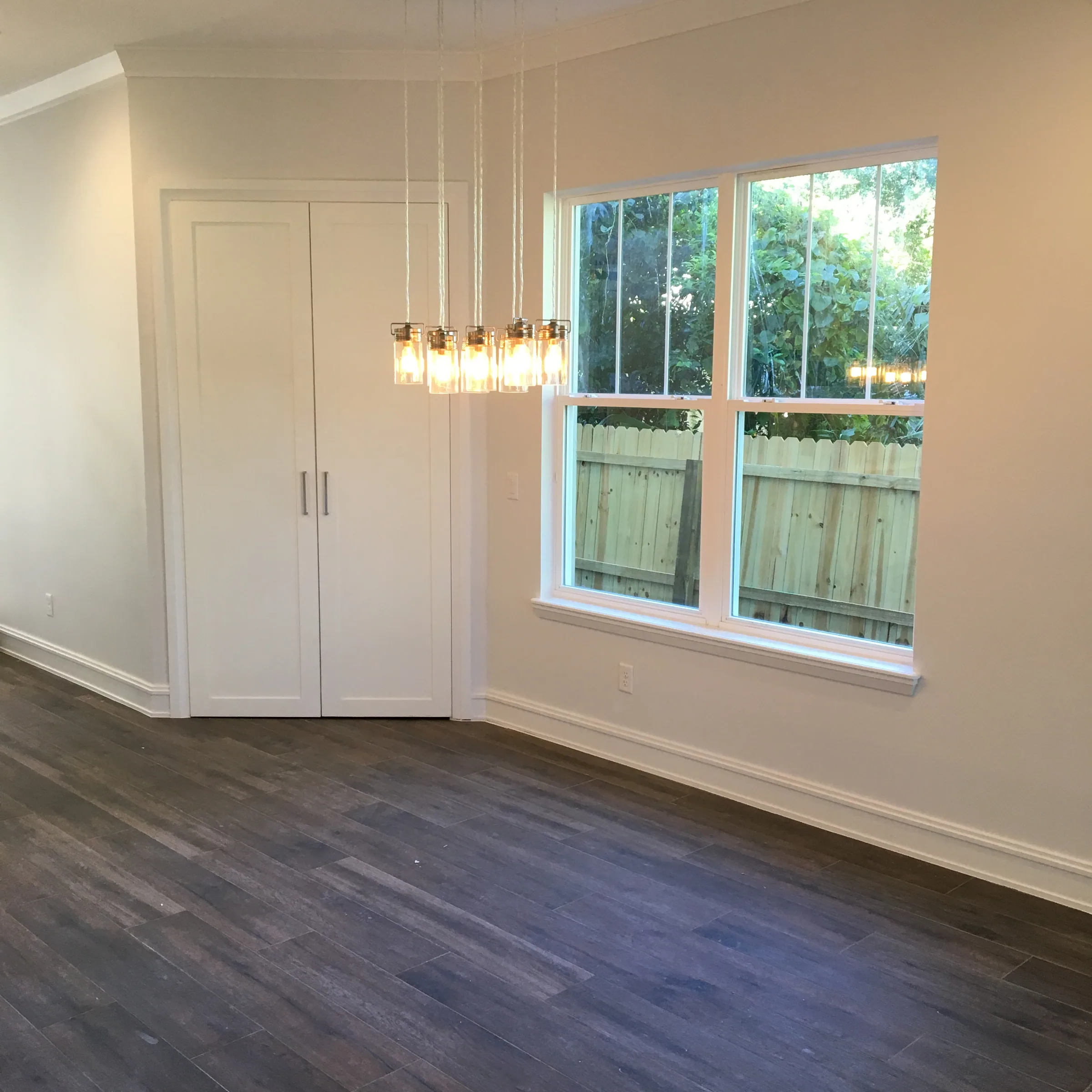 Glass pendant lights hang in a dining area beside paired windows and white double doors.