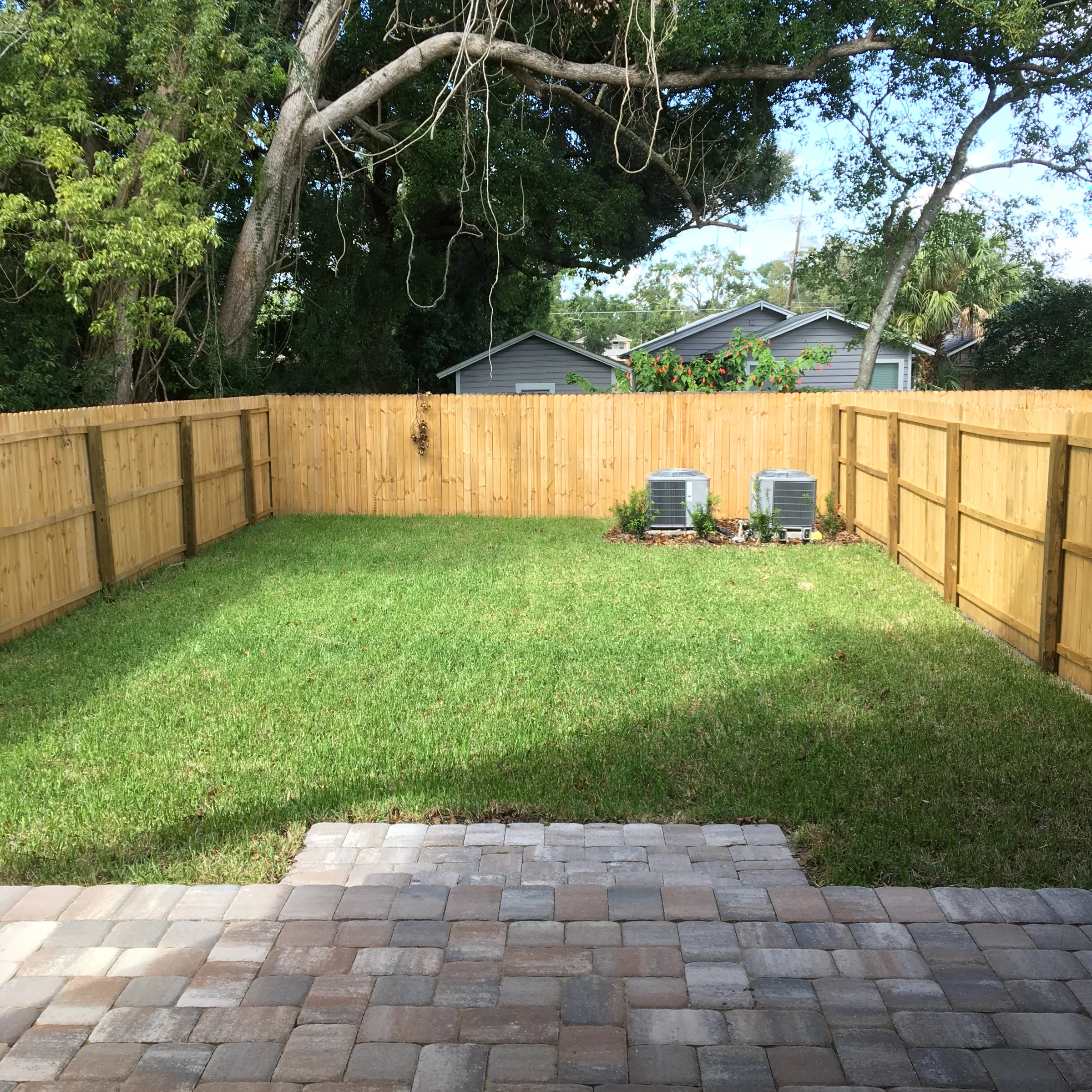 Fenced rear lawn at East Evans with a paved patio and mature trees beyond the fence.