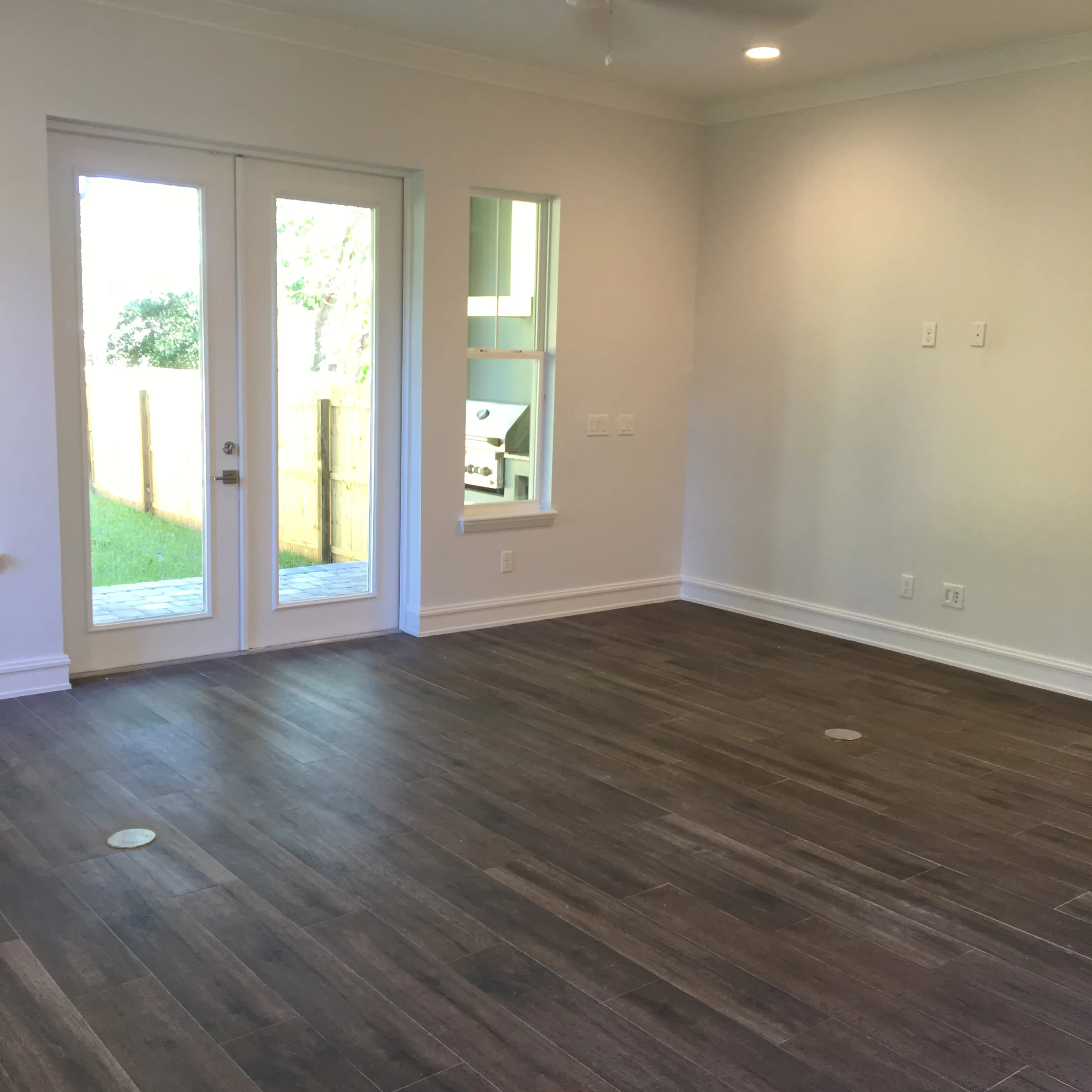 An unfurnished living area with wood-look flooring and glazed double doors opening toward the rear lawn.
