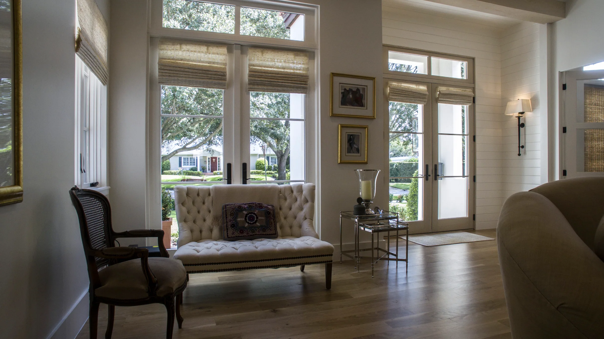 Front sitting area with tall glazed openings, transom windows, pale ceiling beams and a tufted settee.