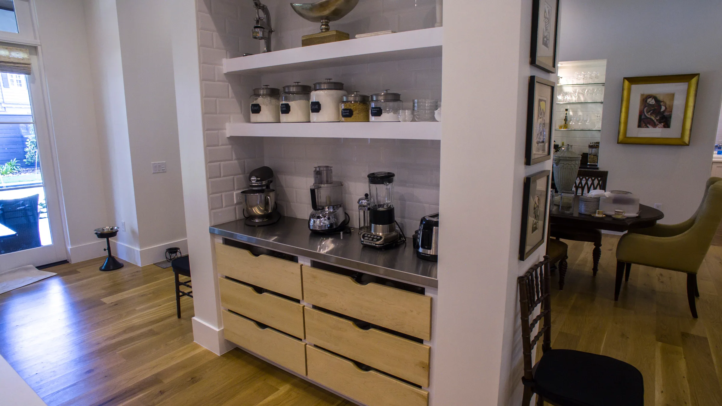 Recessed kitchen alcove with open shelves, a small-appliance counter and wood-grain drawers beside the dining area.
