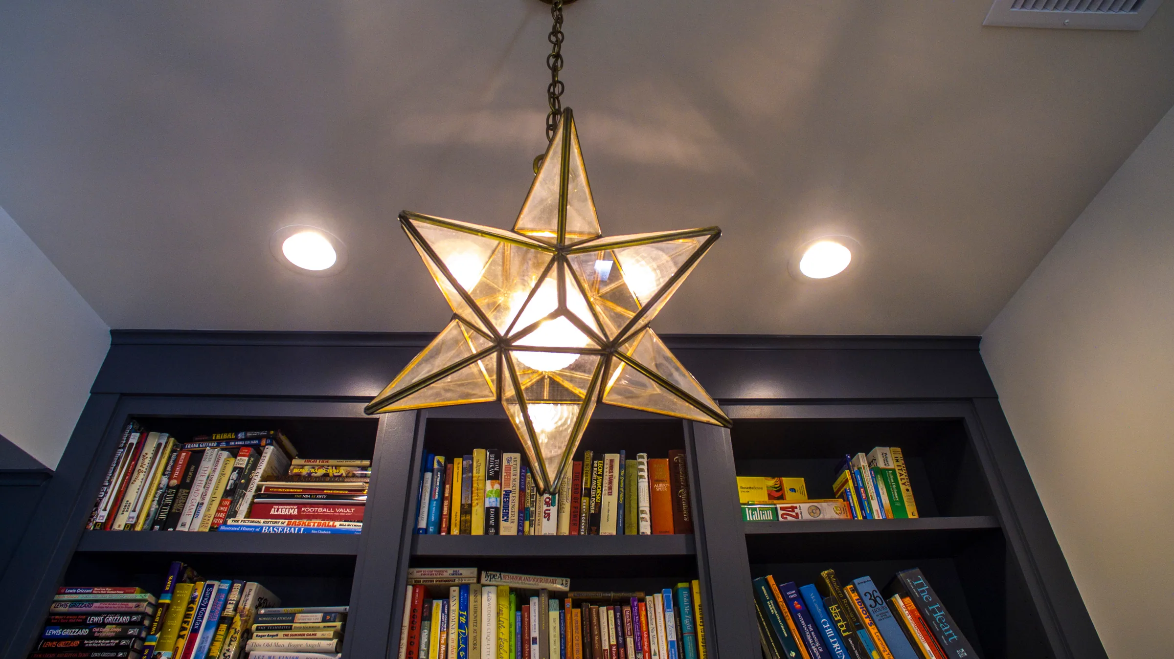 Star-shaped pendant light in front of dark bookshelves beneath a pale ceiling.