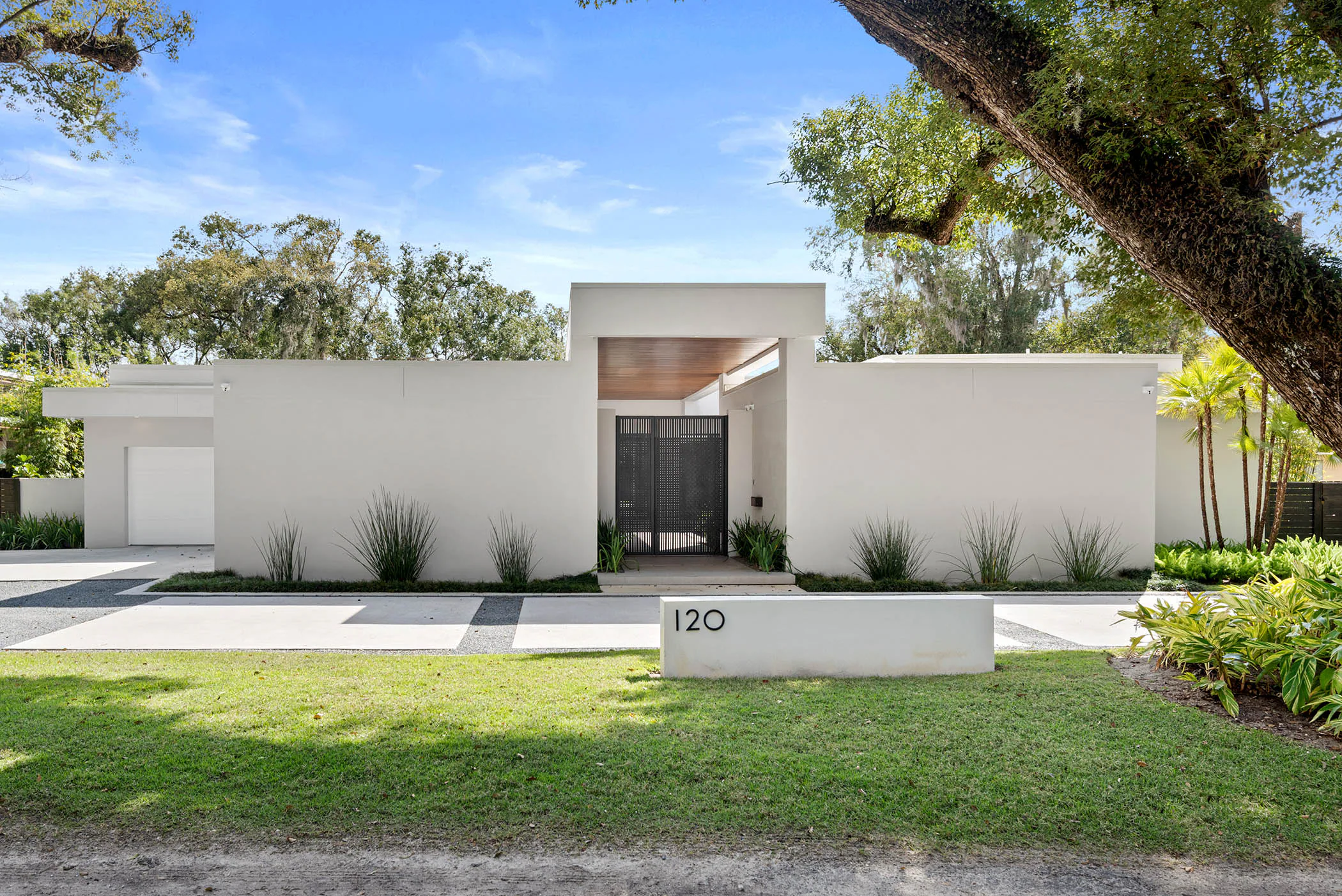 Street elevation of Spring with white stucco, a recessed wood-lined entry and a mature oak.