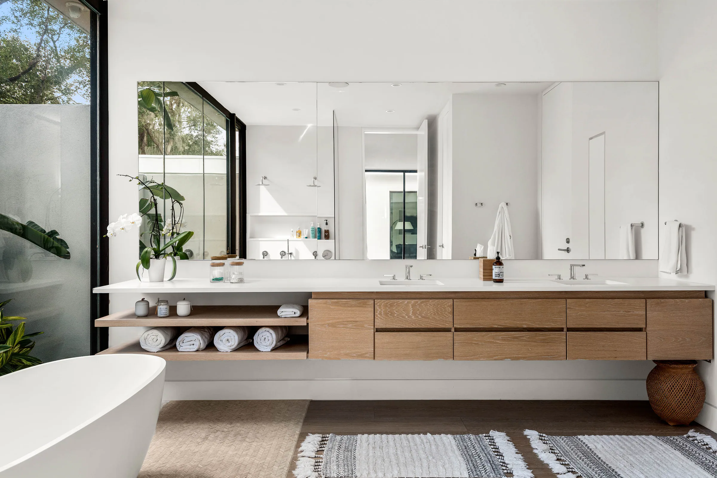 Long wood vanity and freestanding tub beside garden glazing.