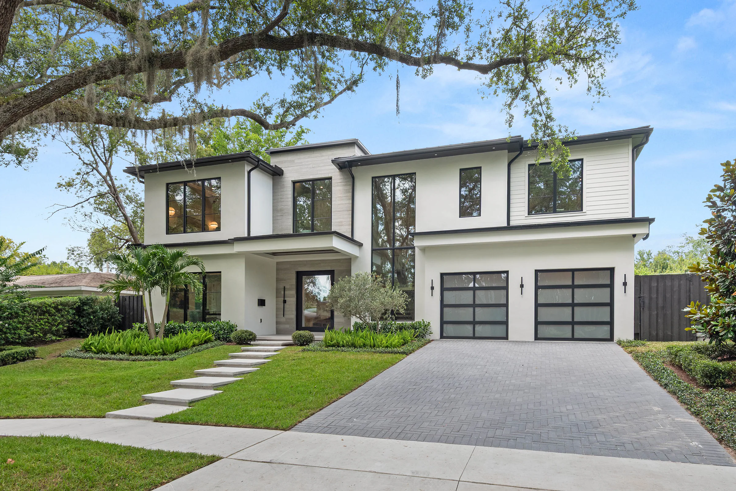 Front elevation of Munster with white stucco, stone, black-framed glazing and layered planting.