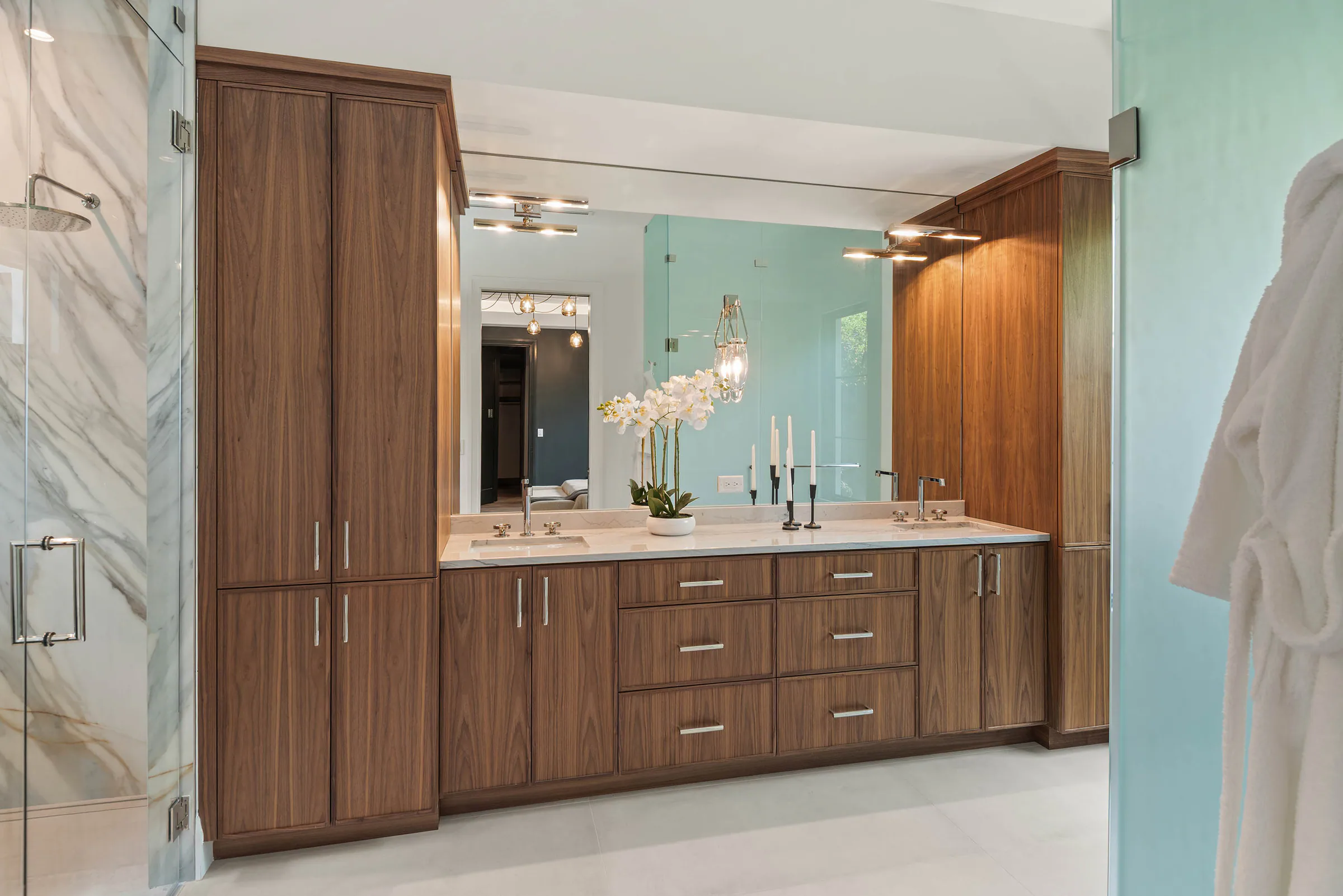 Wood vanity and veined stone wall beneath warm lighting. Munster, a custom home by Rare Builders in Orlando.
