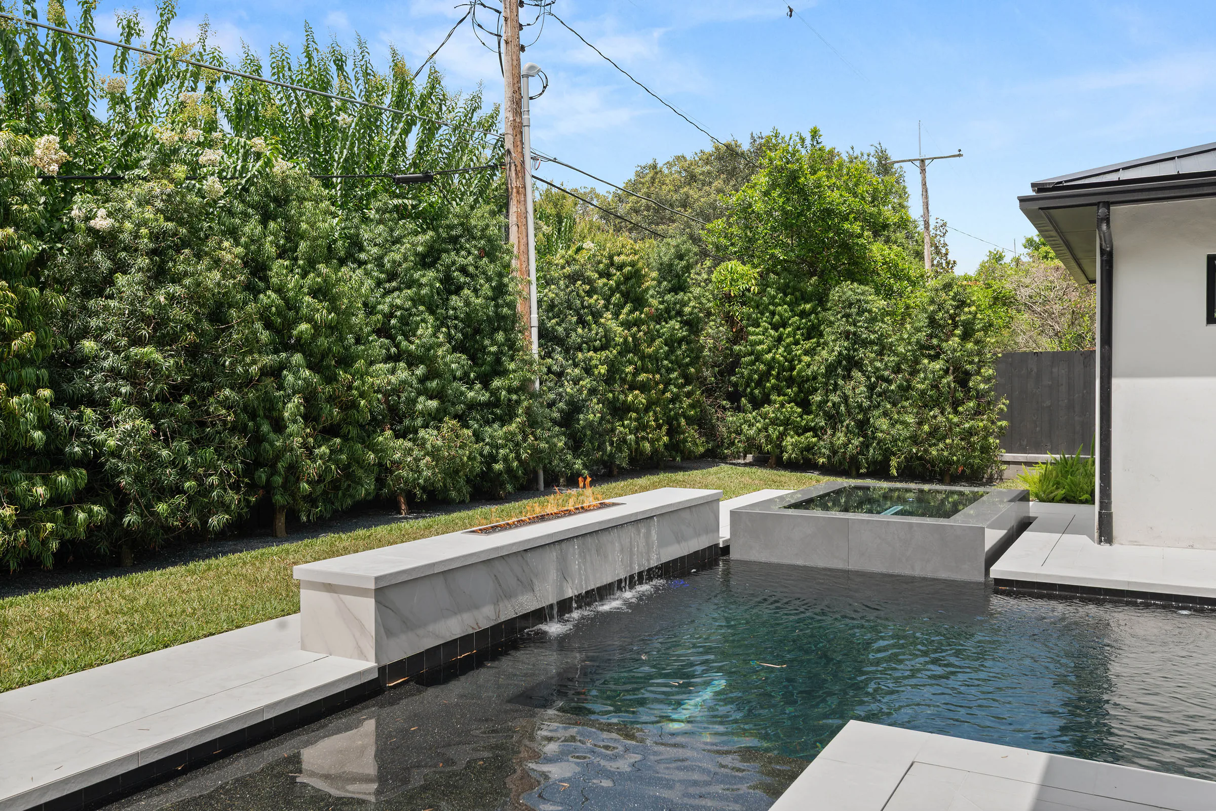Pool and spa edged by dark stone and tall privacy hedges. Munster, a custom home by Rare Builders in Orlando.