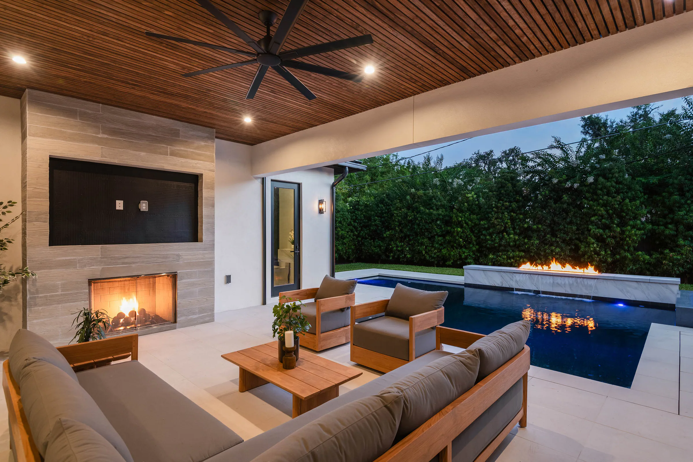 Covered outdoor lounge and pool illuminated at night. Munster, a custom home by Rare Builders in Orlando.