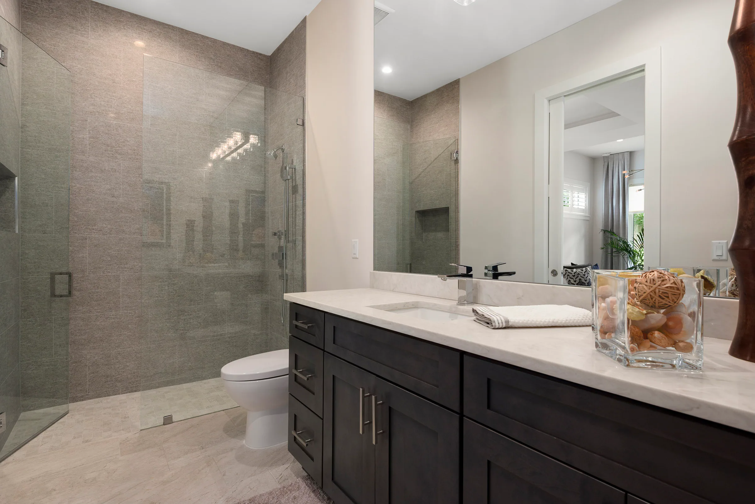 Glass shower lined with warm grey stone tile.