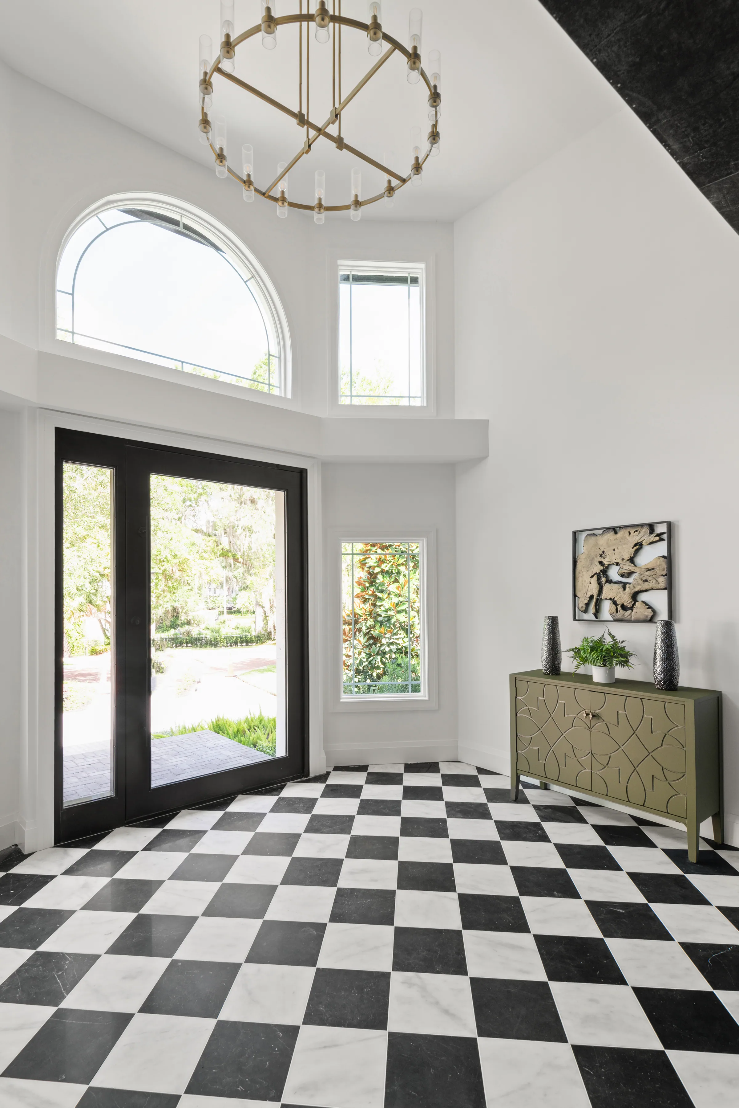 Tall foyer with a black-and-white checkerboard floor, glazed double entry doors and an arched upper window.