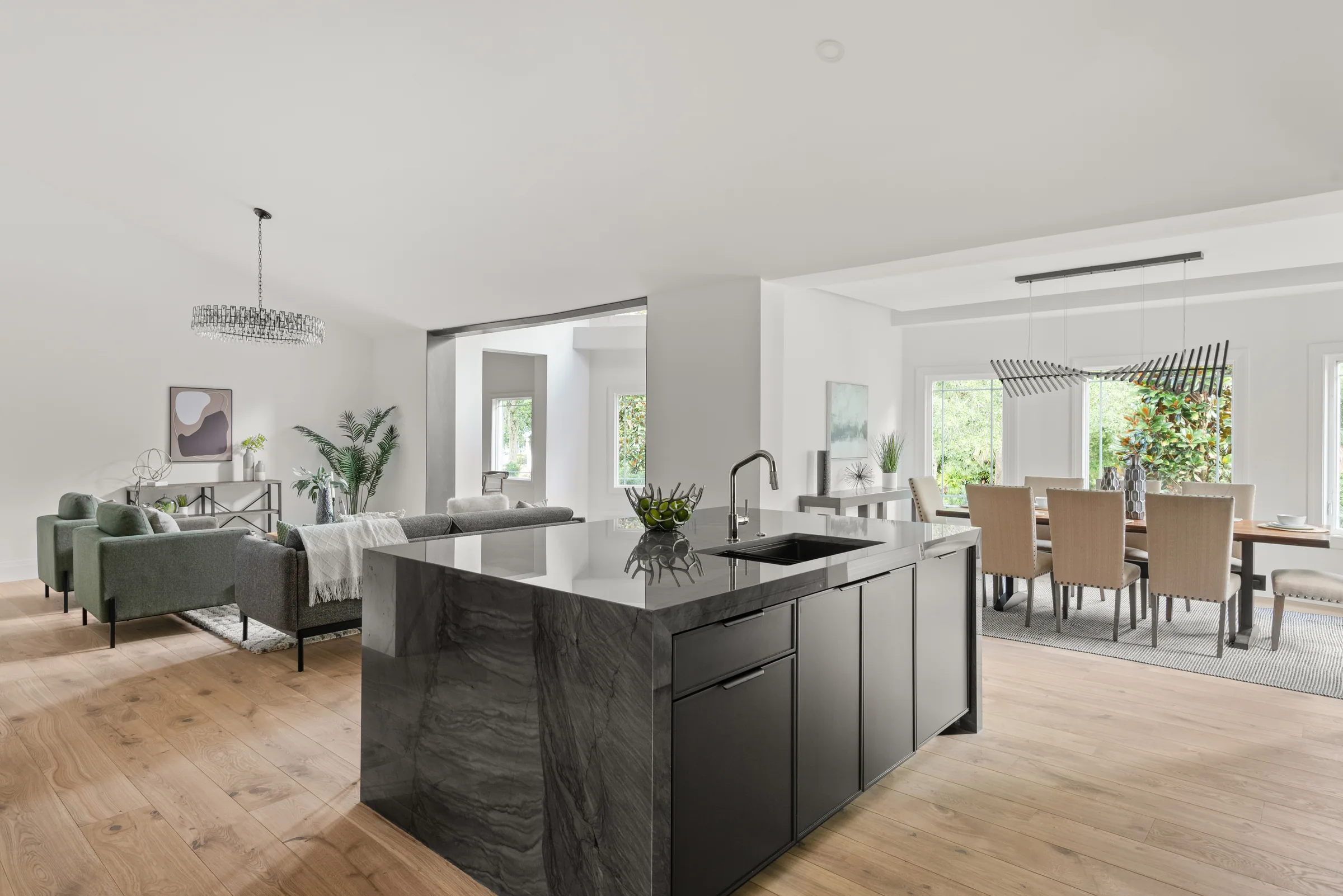 Dark kitchen island with a pale countertop beside open living and dining areas and garden-facing glazing.