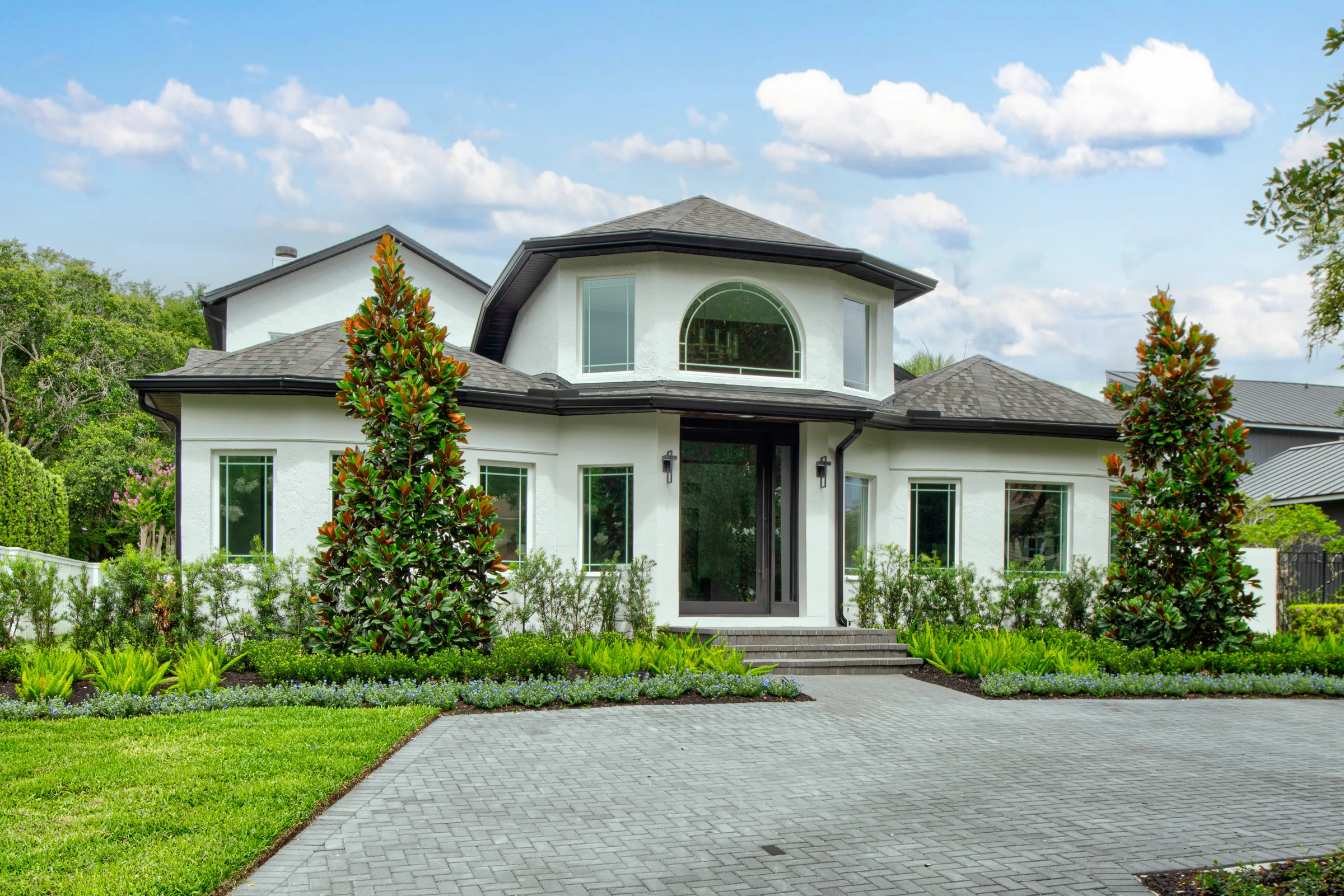 White Lakeview residence with a central arched upper window, dark entry columns and a landscaped paver approach.