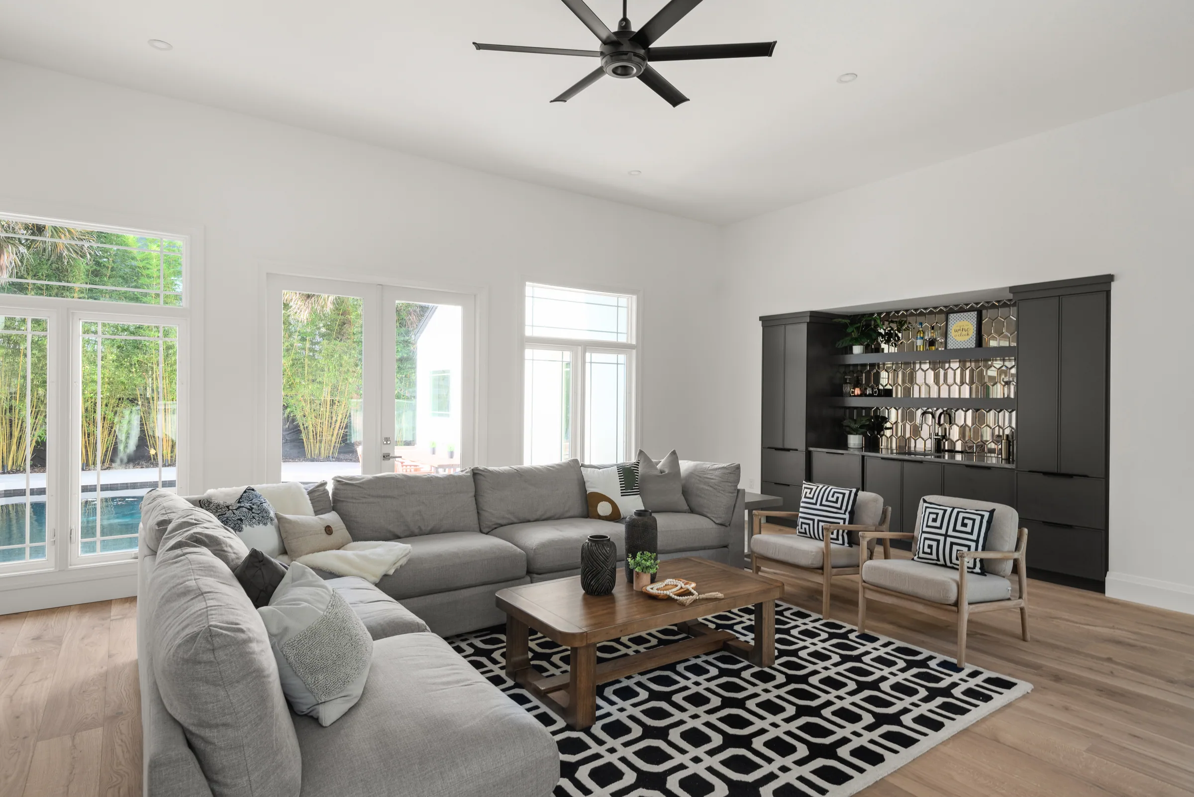 Bright lounge with a gray sectional, dark built-in shelving and broad windows overlooking greenery.