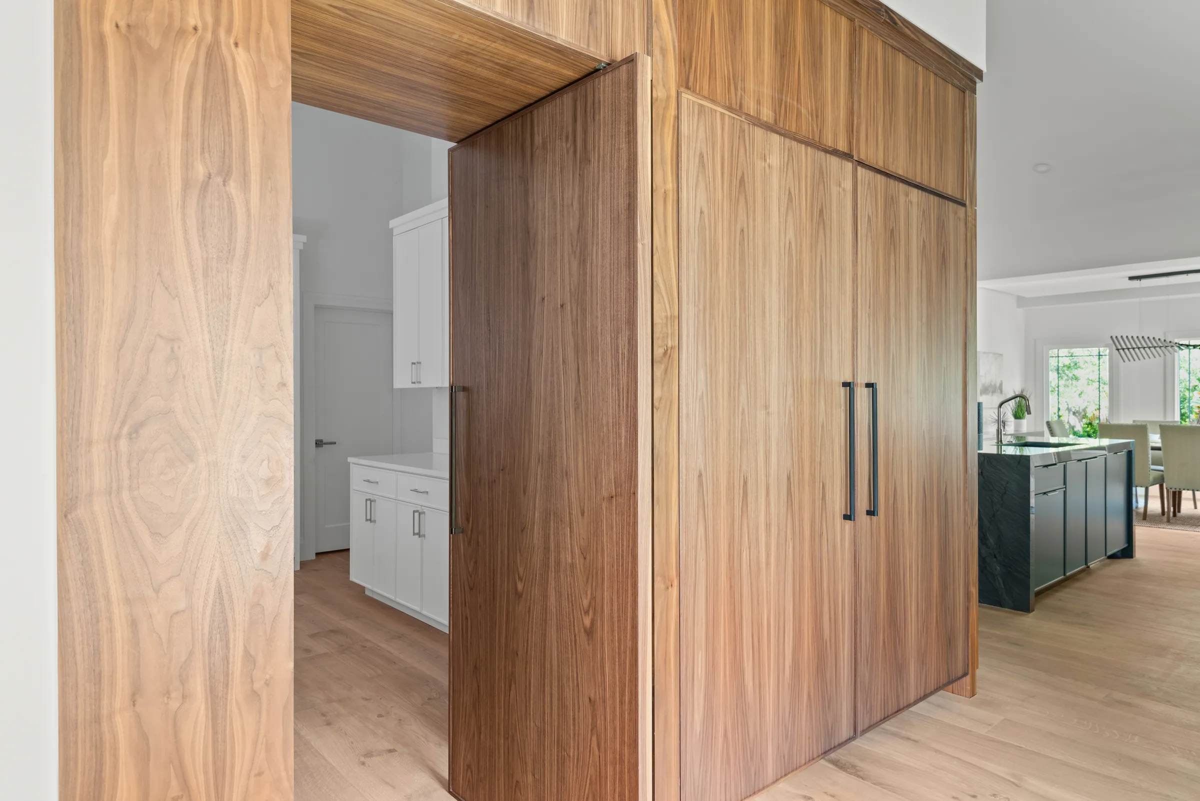 Full-height wood cabinetry framing an open doorway into a white pantry beside the kitchen.