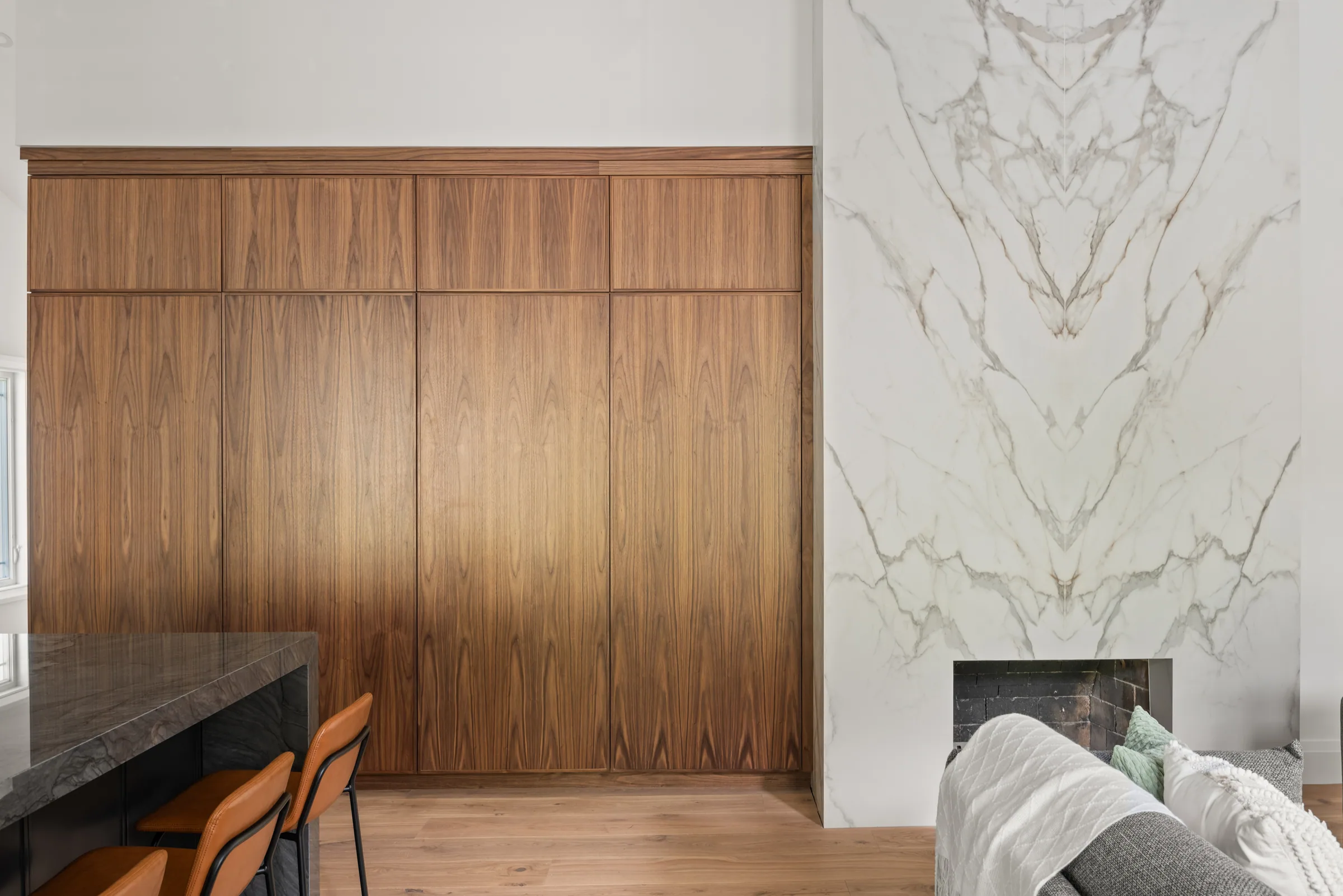 Wood cabinetry and a tall pale veined fireplace surround beside the kitchen island and living area.