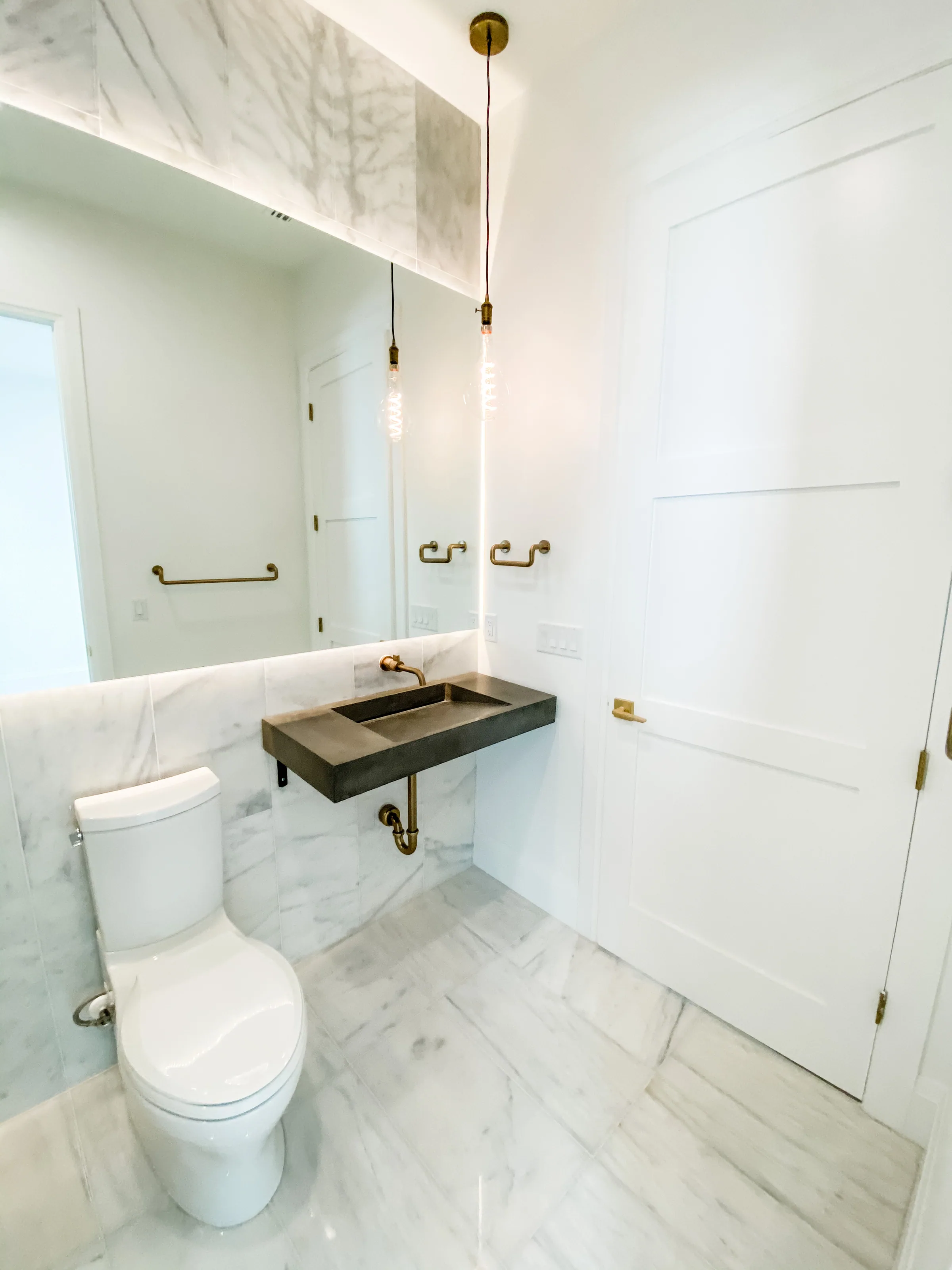 Westmoreland bathroom with a dark wall-mounted basin, veined wall surfaces and brass-toned fixtures.