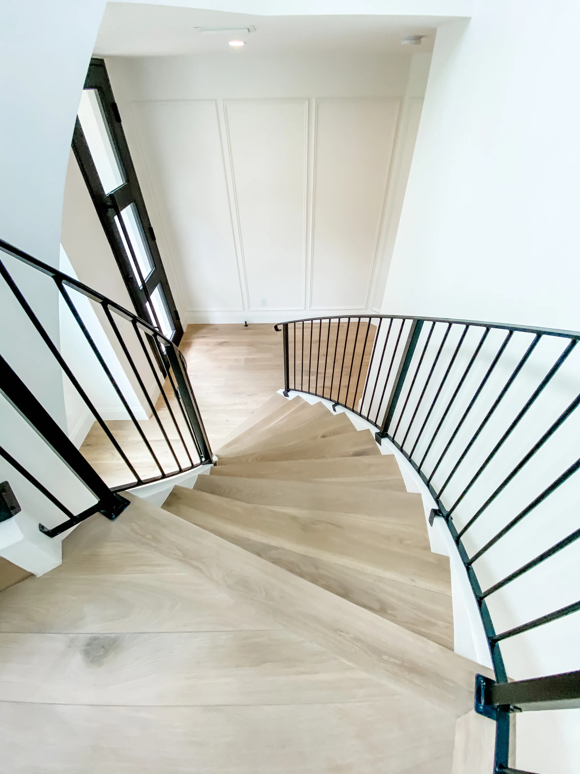 Curved Westmoreland staircase viewed from above, with pale wood treads and dark vertical metal railings.