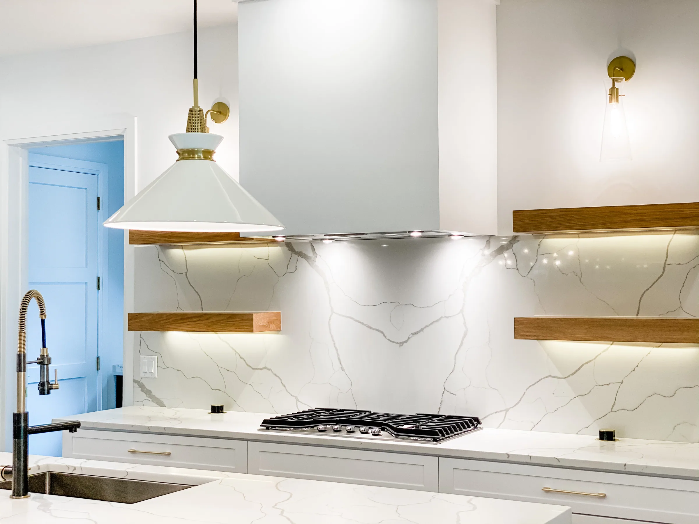 White kitchen hood and veined backsplash framed by open wood shelves at Westmoreland.