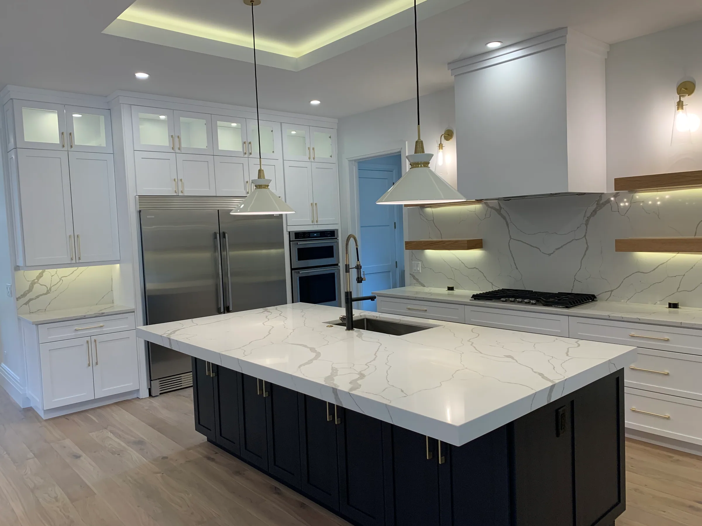 Westmoreland kitchen with white perimeter cabinets, dark island, veined countertop and pendant lights.