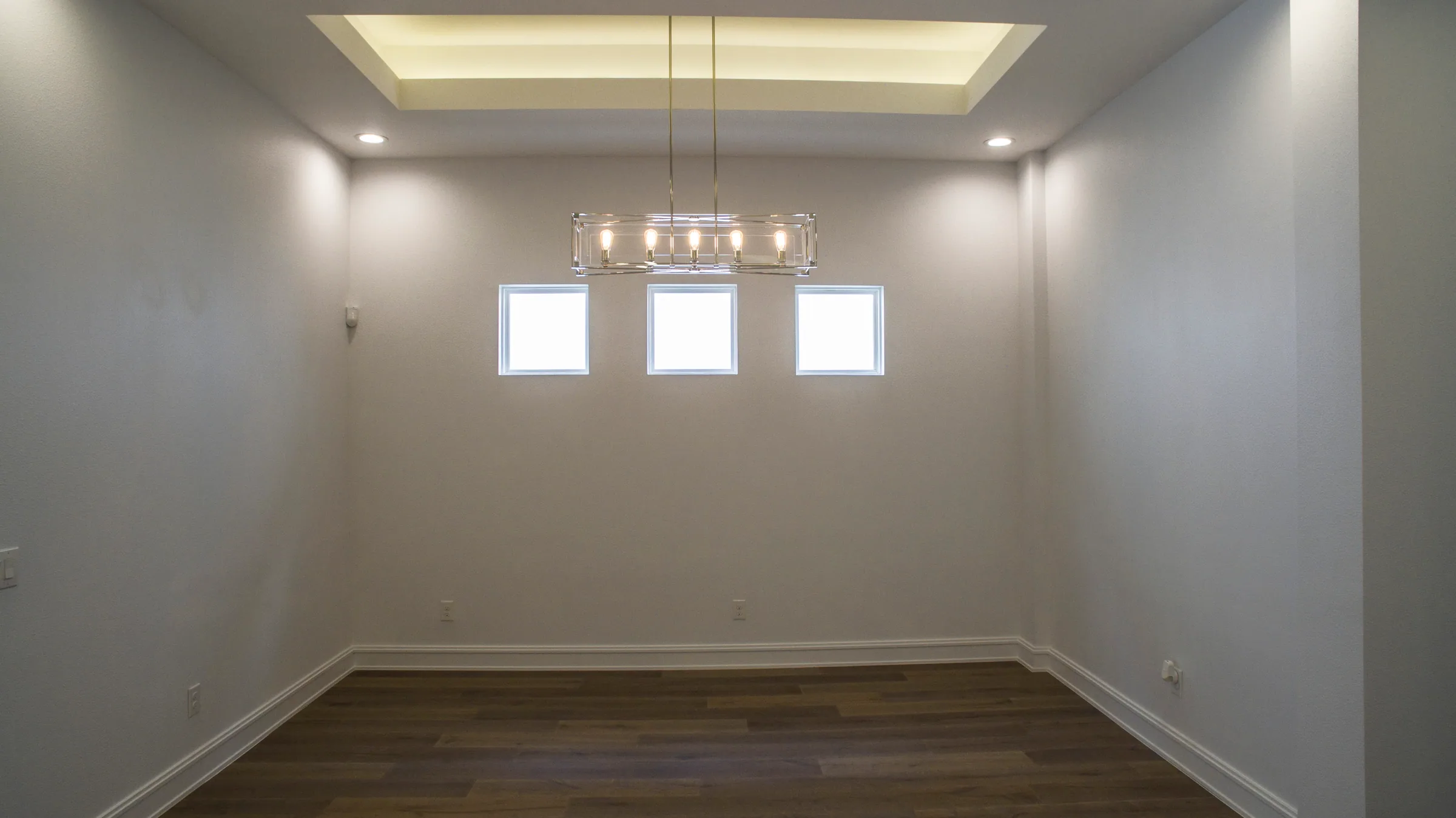 Dining room with a recessed ceiling, linear chandelier and three high rectangular windows.