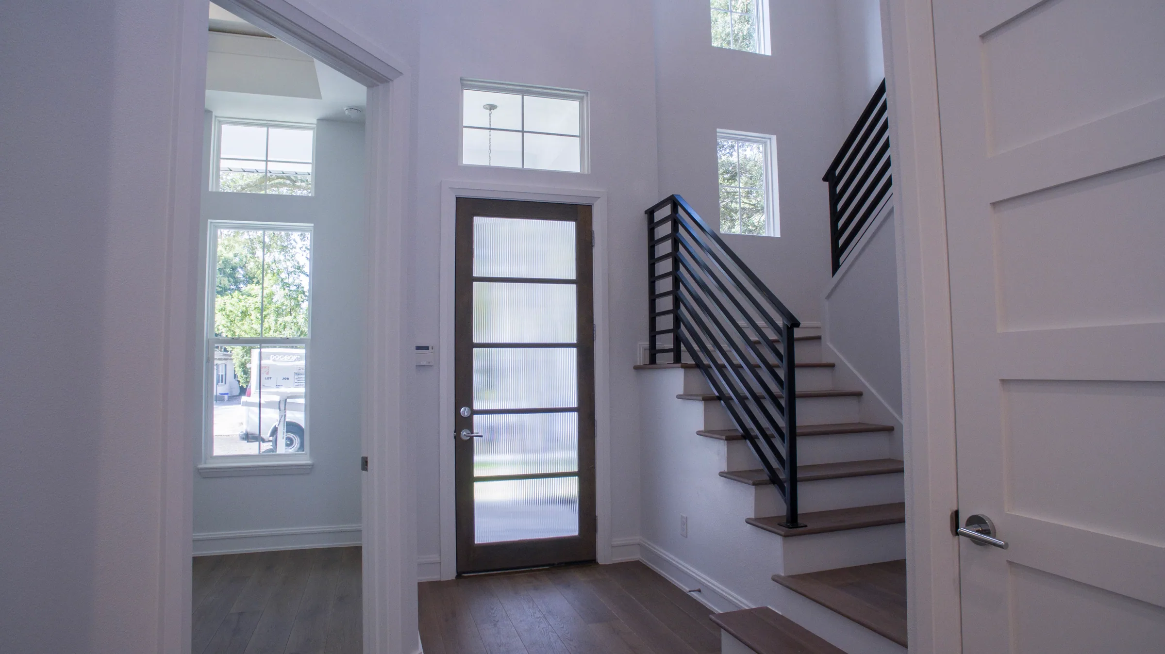 Tall glazed front entrance beside wood-toned stairs with dark horizontal railings and high windows.