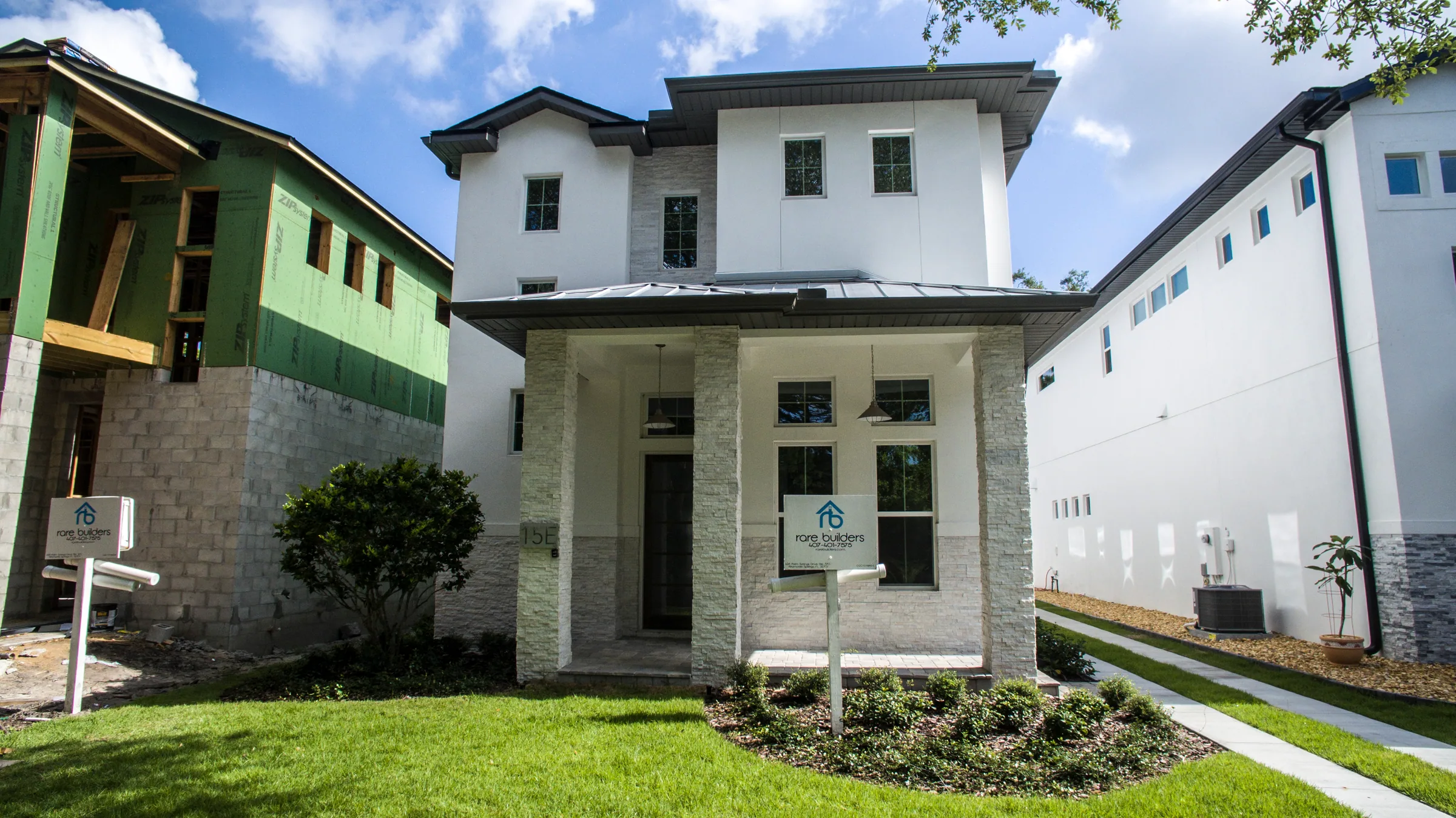 White two-story East Harvard home with a stone-clad front porch, dark entry door and ribbon driveway along the side.