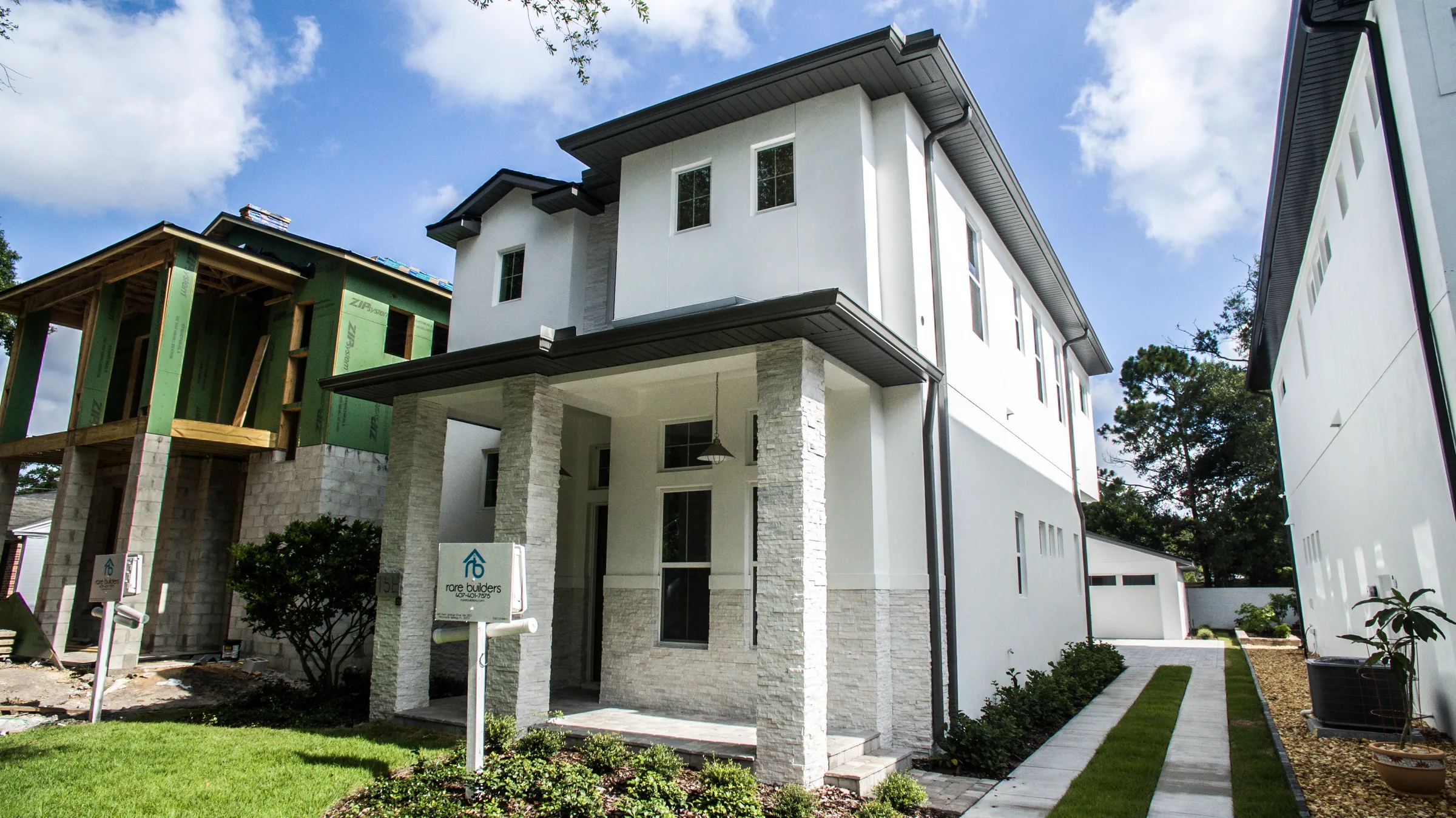 Angled view of the stone-clad porch and white two-story facade beside the ribbon driveway.
