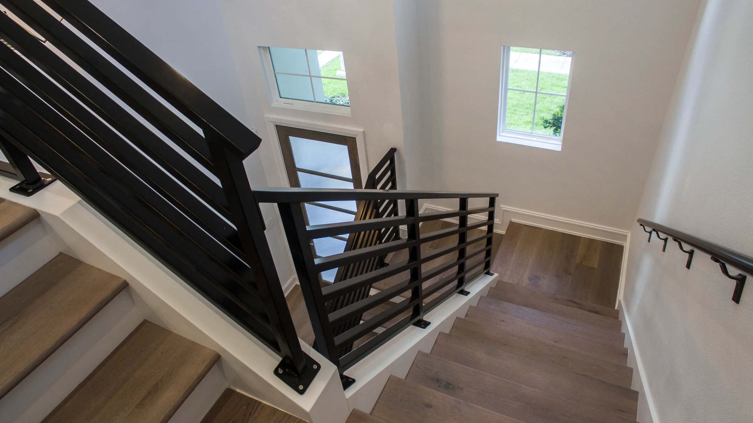 Wood-toned stair landing with dark horizontal railings and high windows illuminating the stairwell.