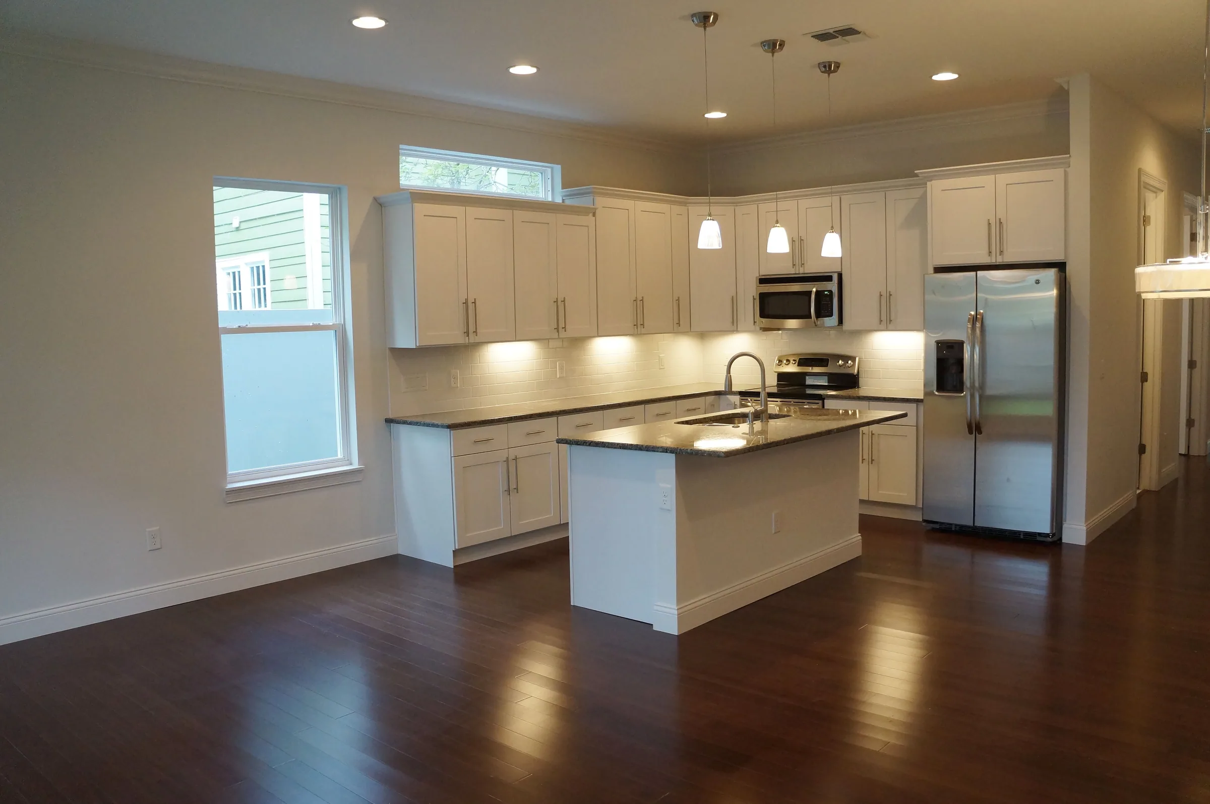 West Harvard kitchen with white cabinets, an island with a sink, high windows and dark flooring.