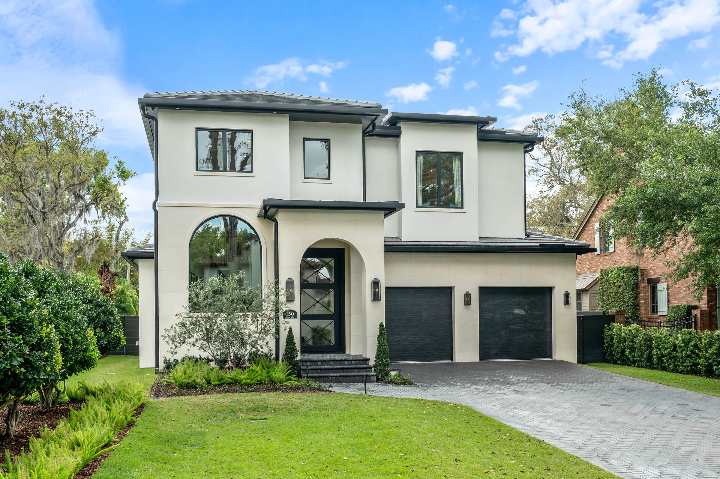 White stucco front elevation with dark garage doors and an arched entry.
