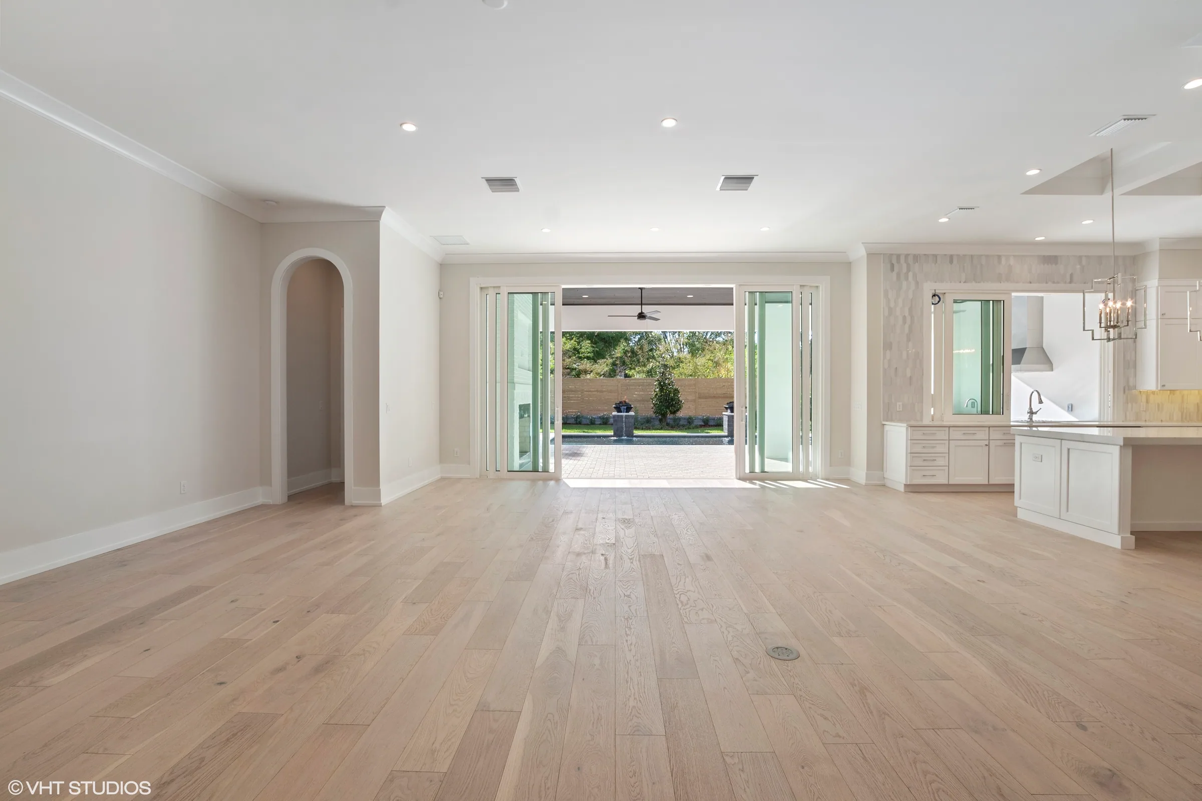 Unfurnished living area with light-toned plank flooring and wide open sliding doors facing a covered patio and pool.