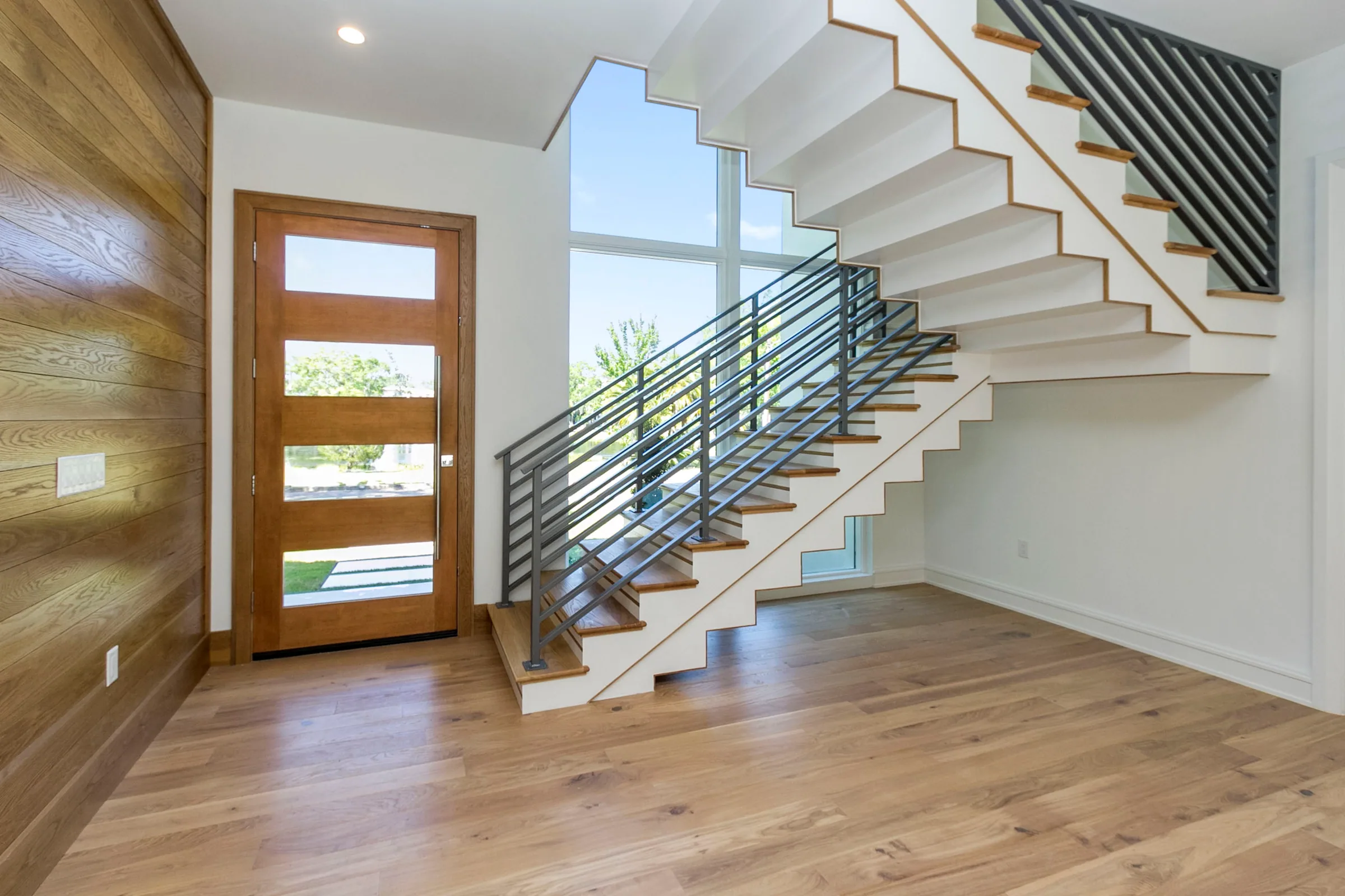Wilbar entry with a folded white stair, wood treads, horizontal dark railings, tall glazing and a wood-clad wall.