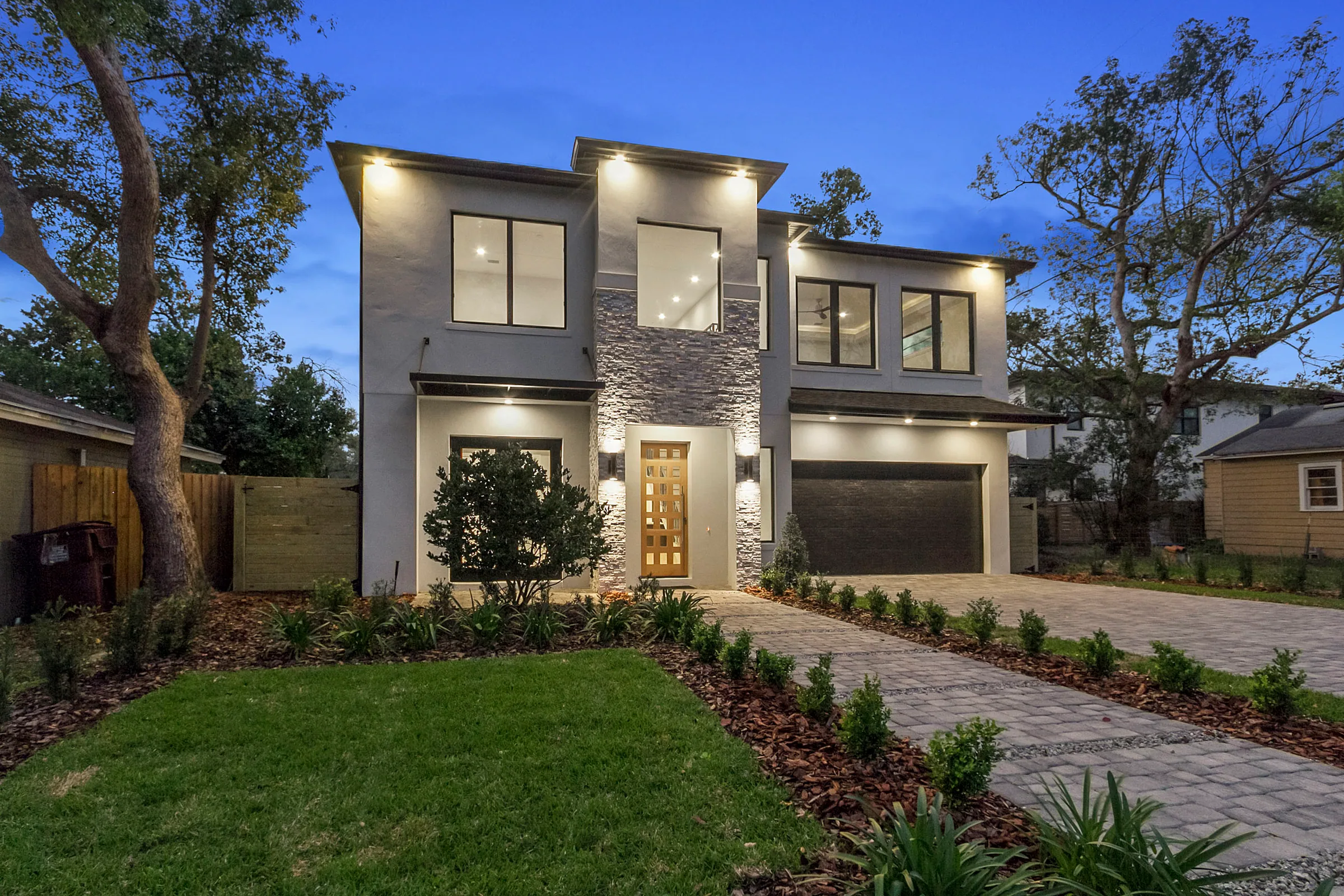 Two-story white home with a stone-textured entry, tall front windows and a dark garage door at dusk.