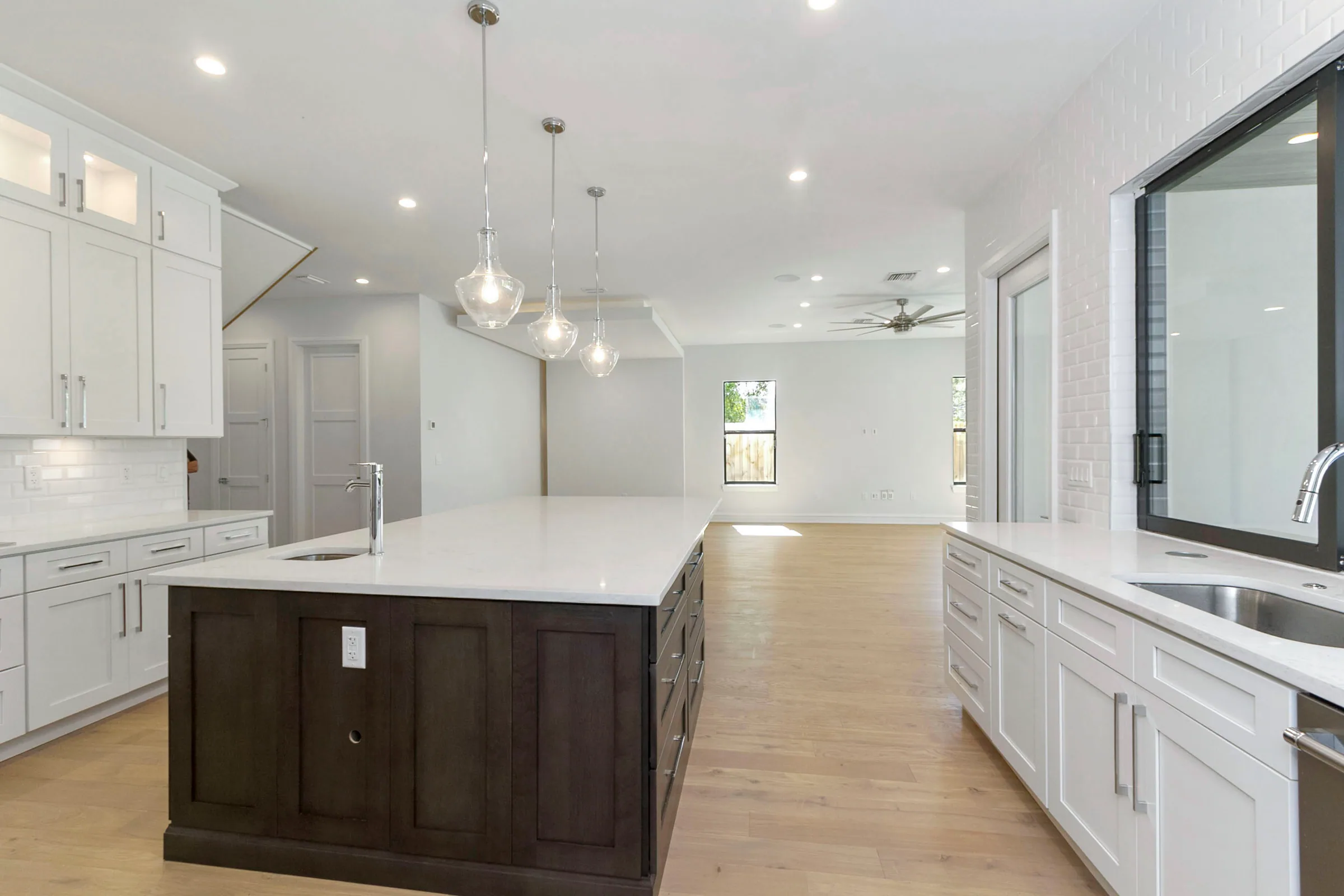 White kitchen with a dark island, three glass pendants and an open view toward the living room.