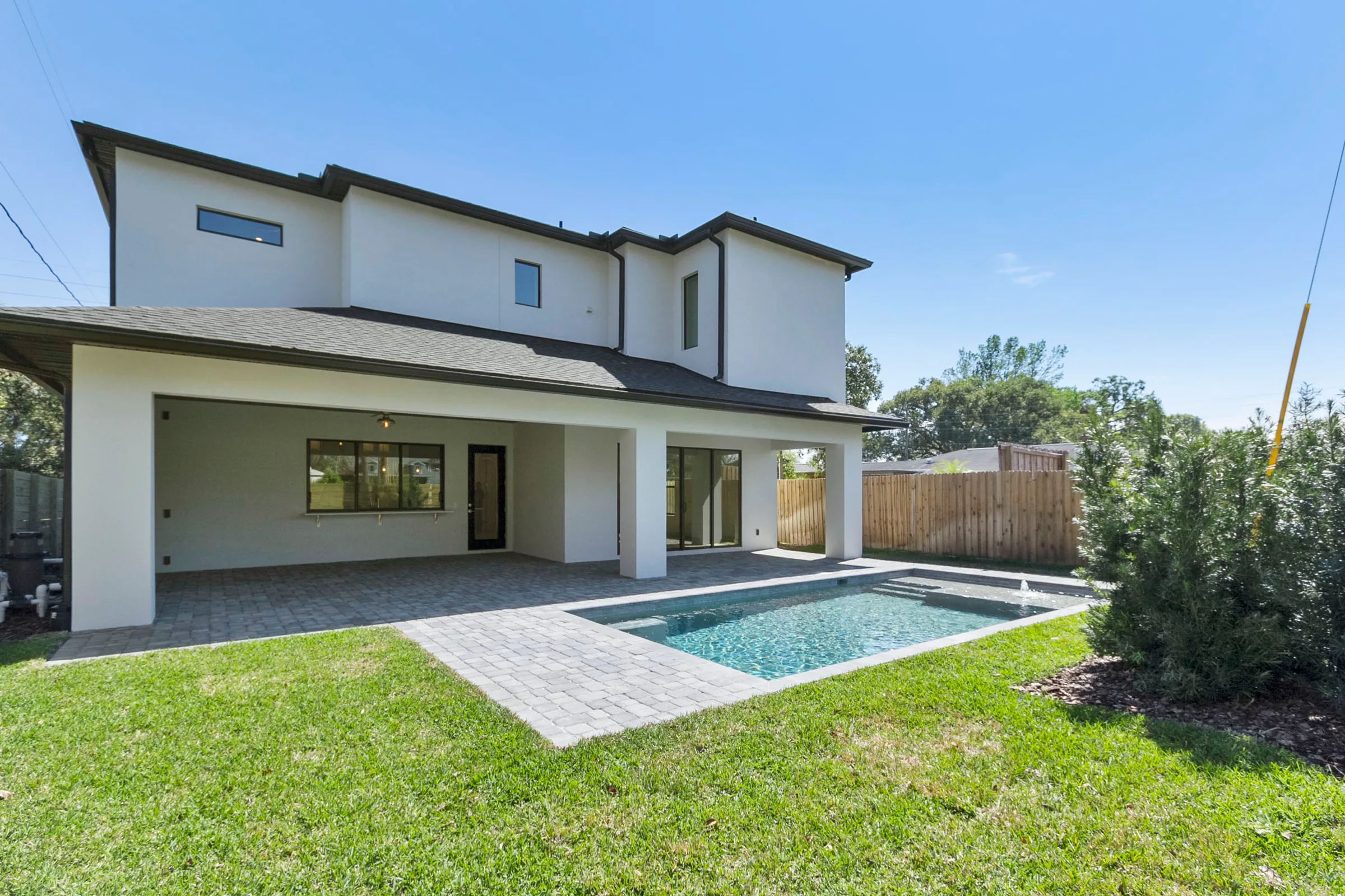 Two-story rear elevation with a covered paved patio, rectangular pool and lawn.