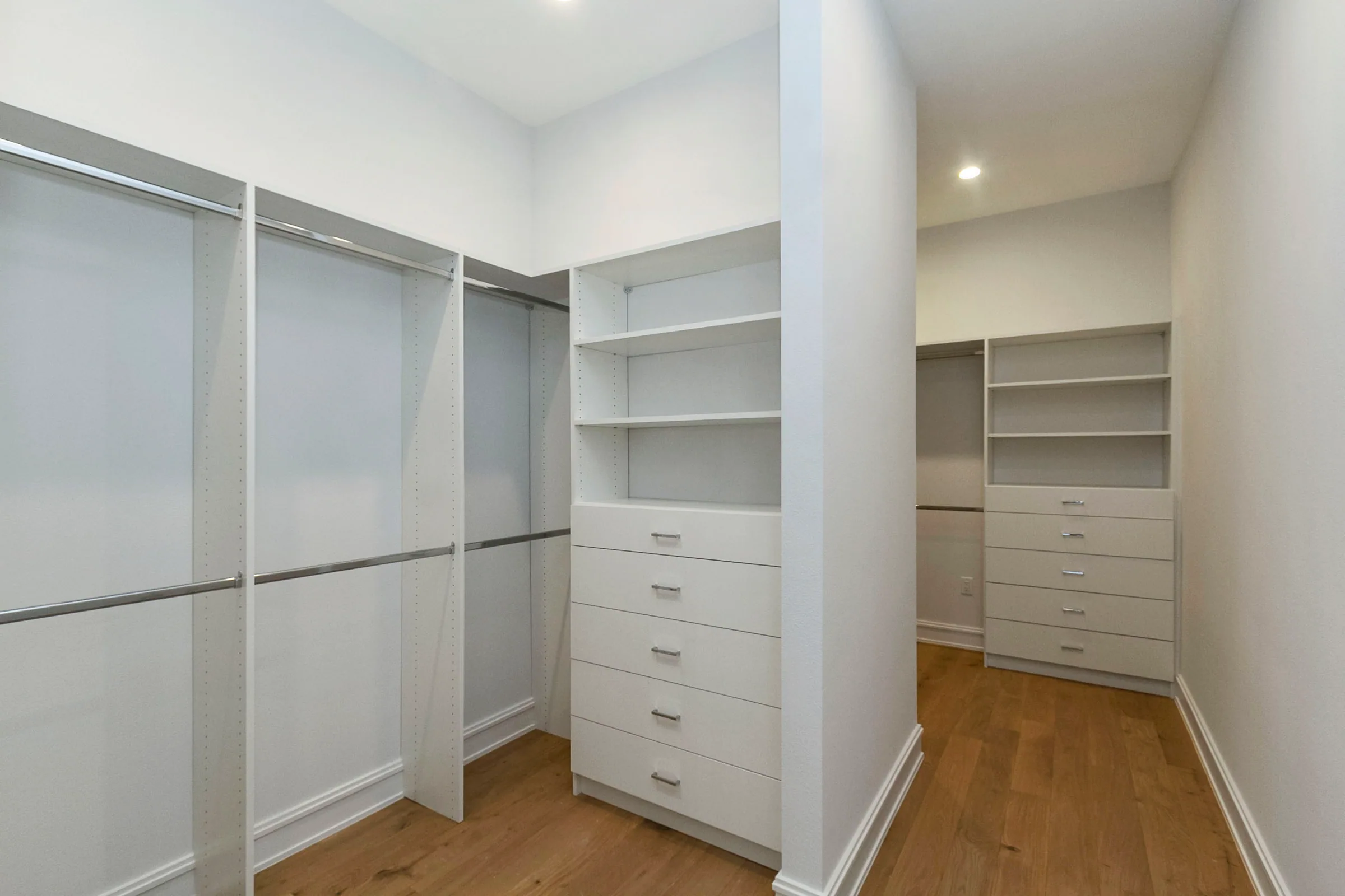Empty walk-in closet with white drawers, open shelves and two levels of hanging rods.