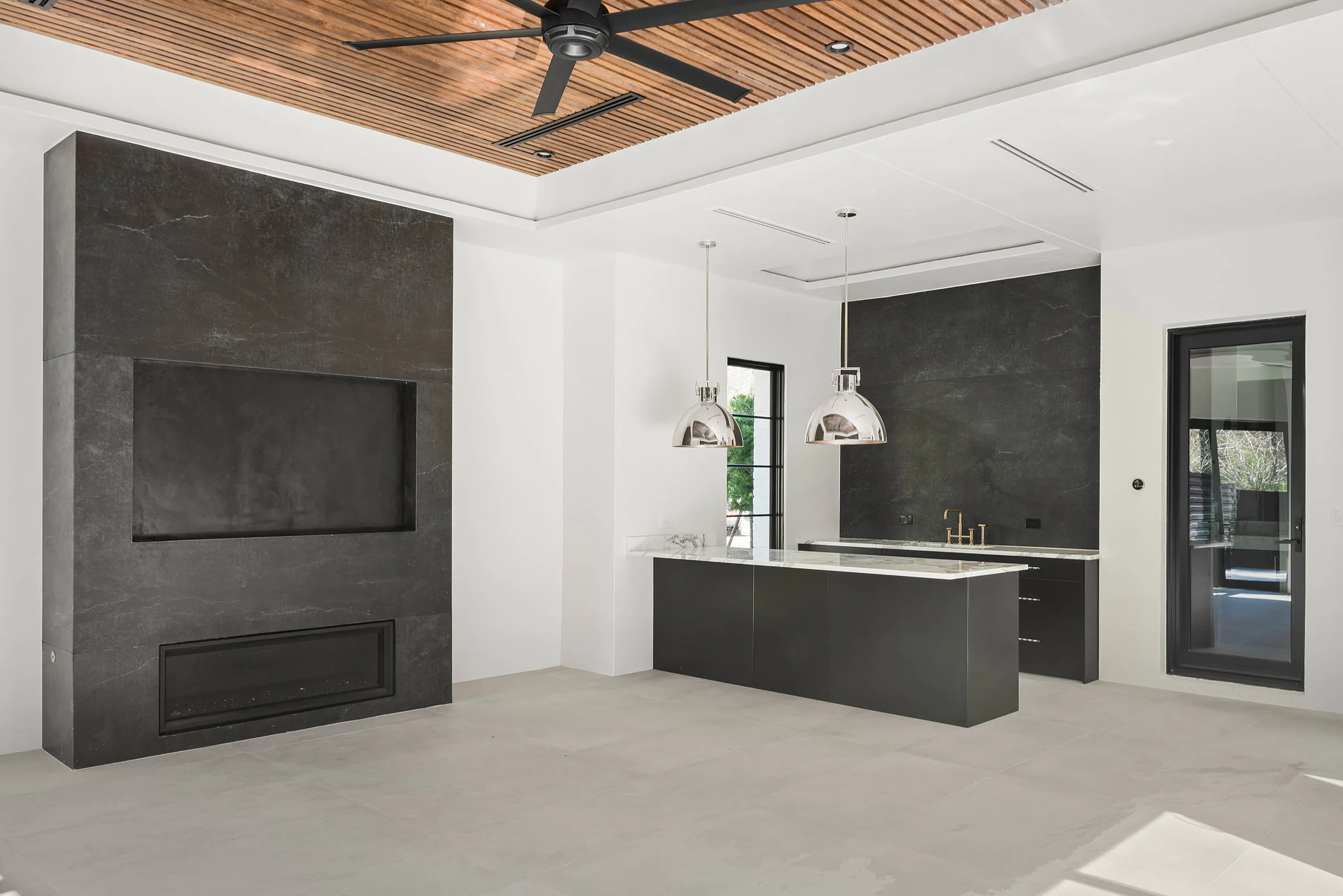 Outdoor kitchen beneath a wood ceiling beside black-framed doors. Oakwood, a custom home by Rare Builders in Orlando.