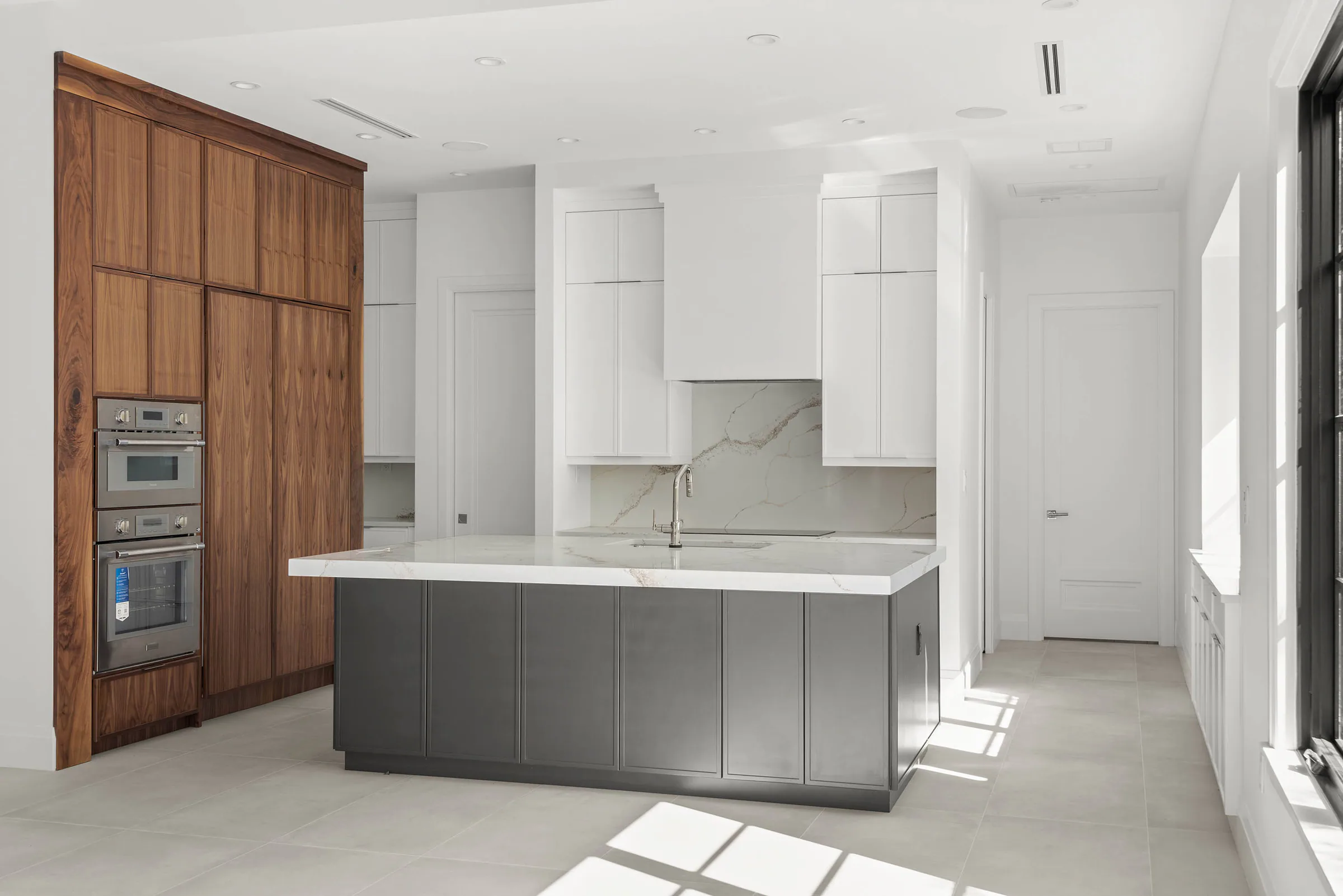 Kitchen island and tall wood storage wall in the bright open interior. Oakwood, a custom home by Rare Builders in Orlando.