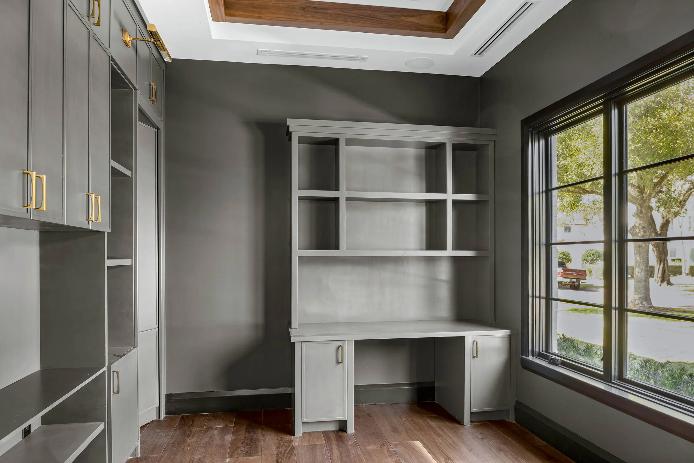 Home office with grey built-in cabinetry, a desk and a corner window.