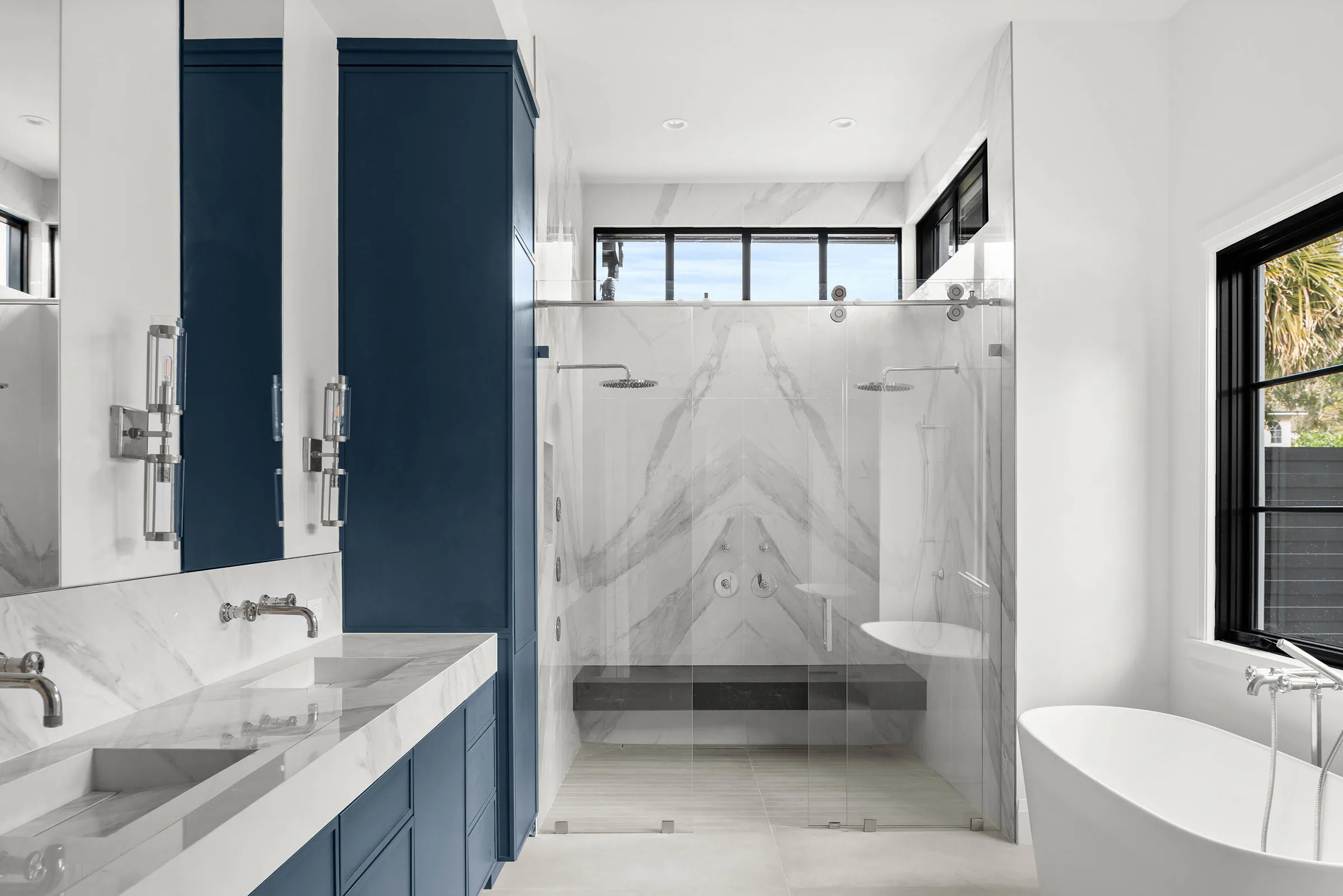 Bathroom with blue vanity, glass shower and freestanding tub.
