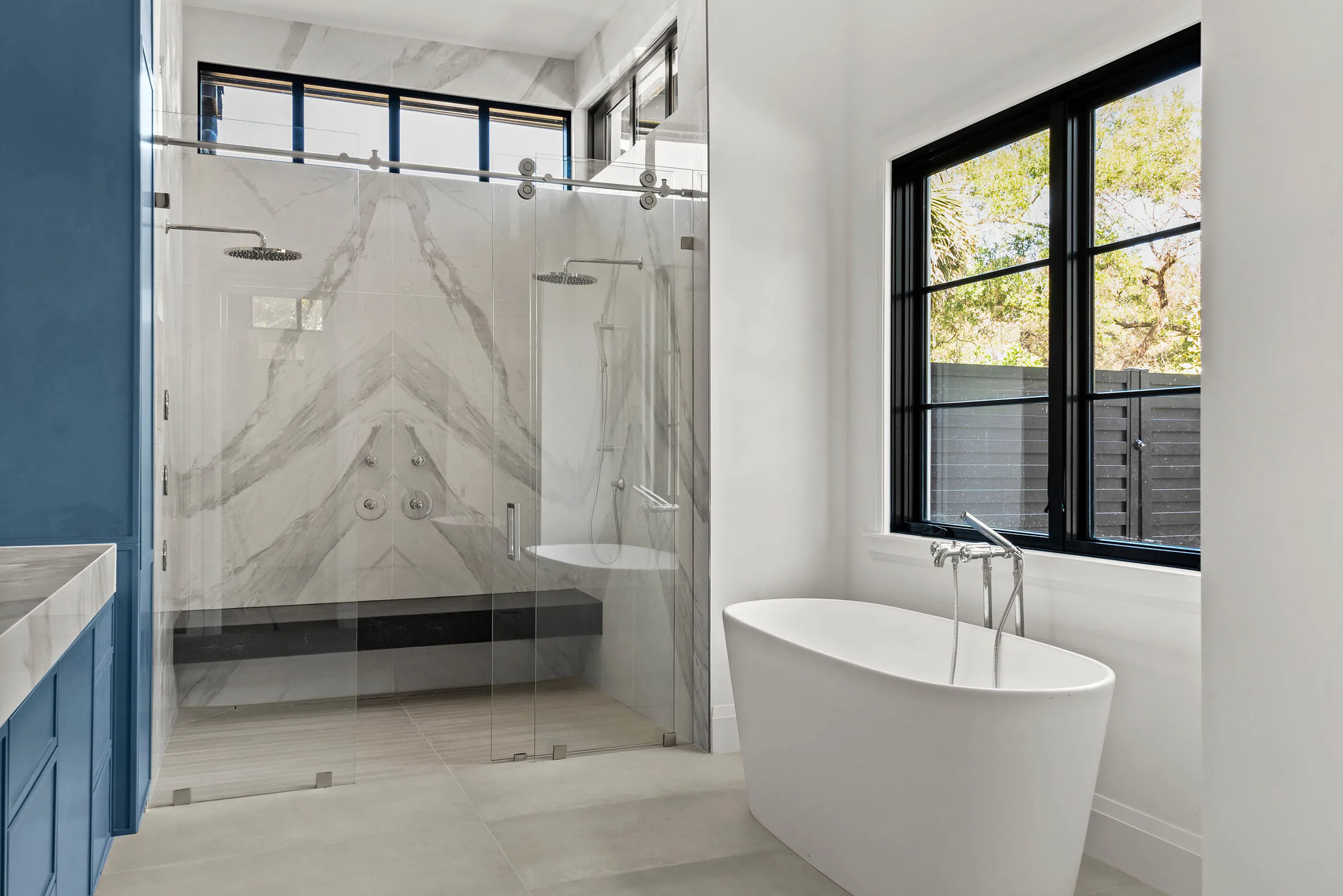 Freestanding tub beside a black-framed window and marble shower. Oakwood, a custom home by Rare Builders in Orlando.