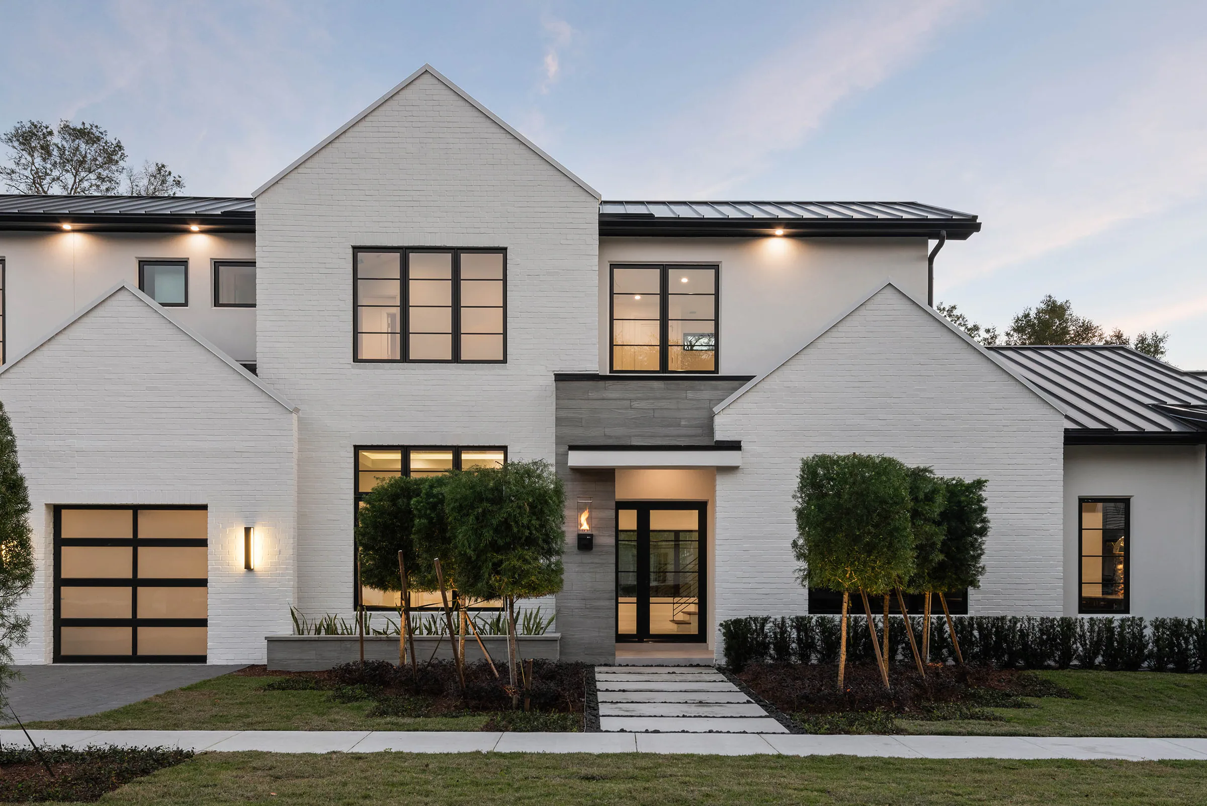Rear elevation with black-framed doors at dusk.