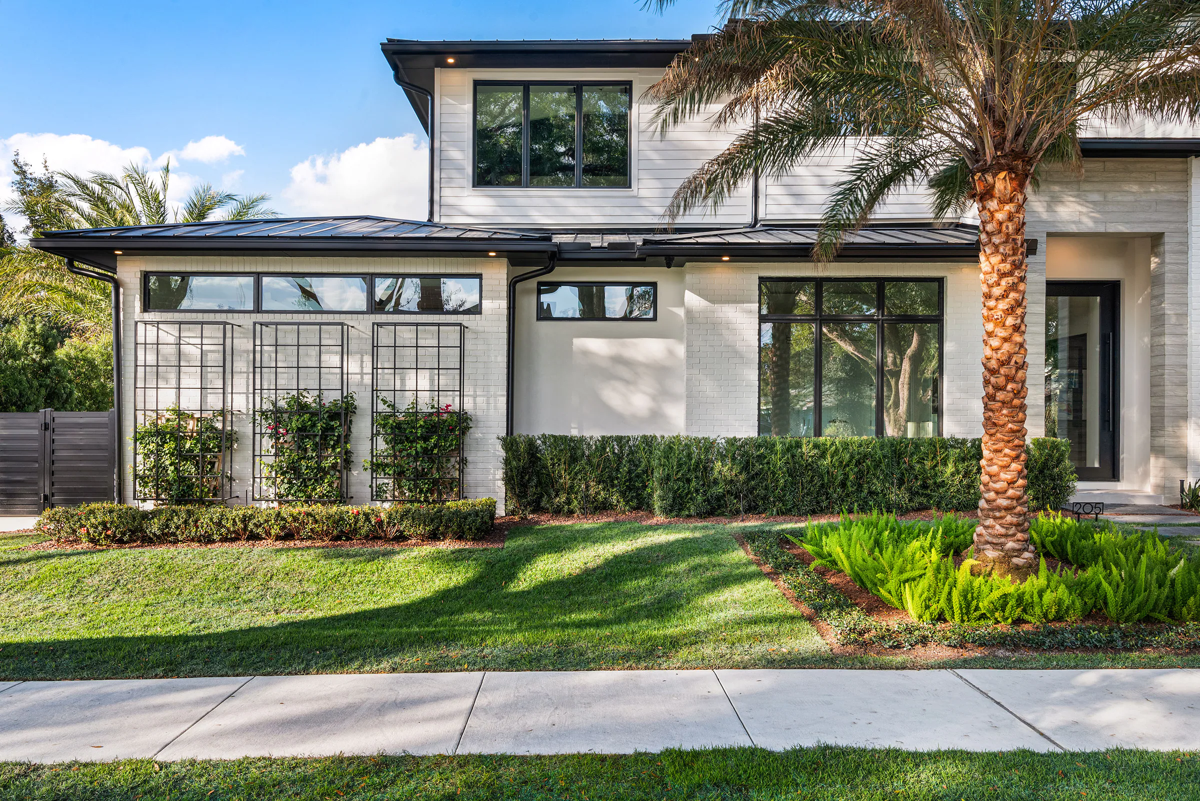 Front elevation framed by lawn, palms and mature live oaks.
