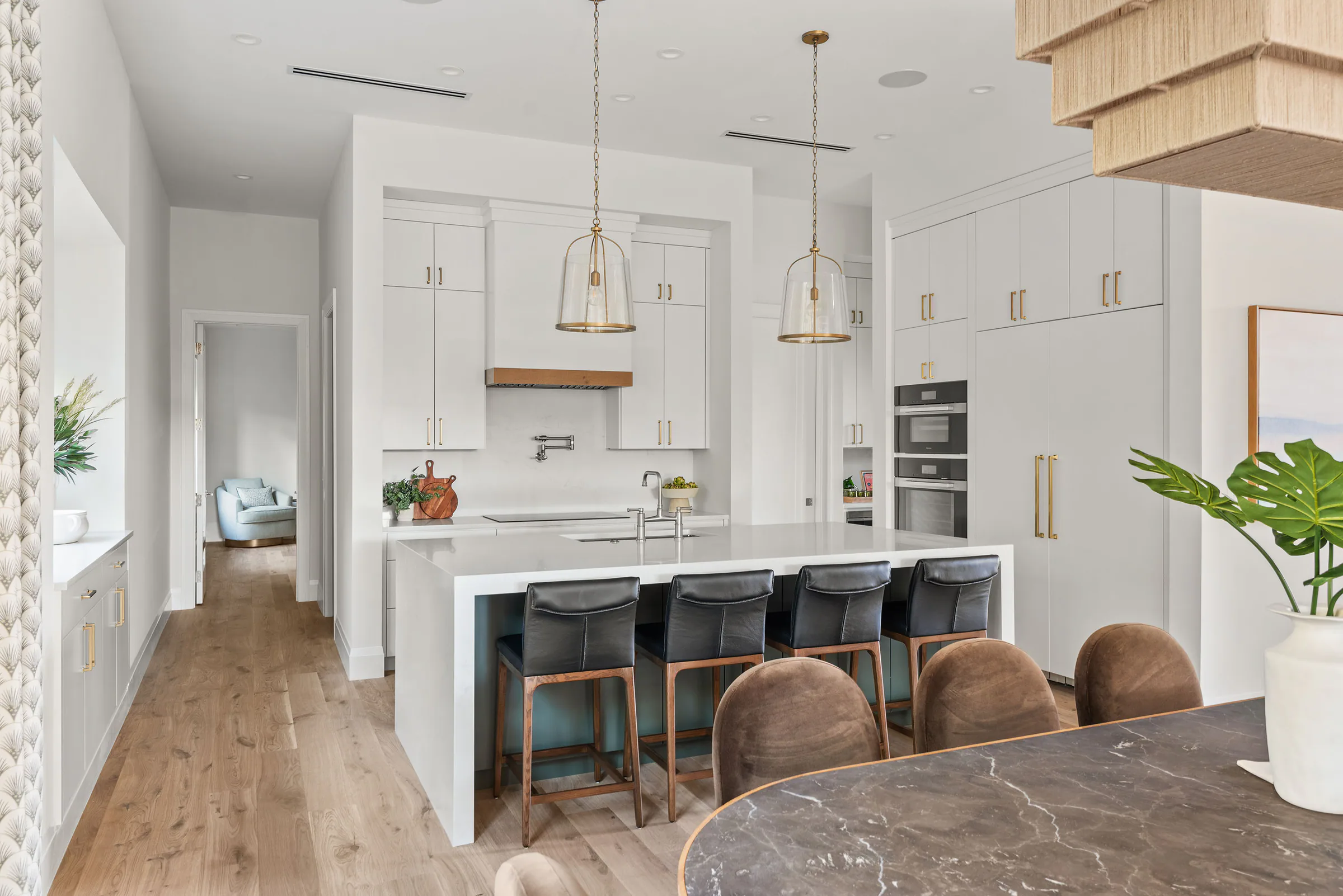 White kitchen with a long island, pendant lights and pale oak flooring. Rockwood, a custom home by Rare Builders in Orlando.
