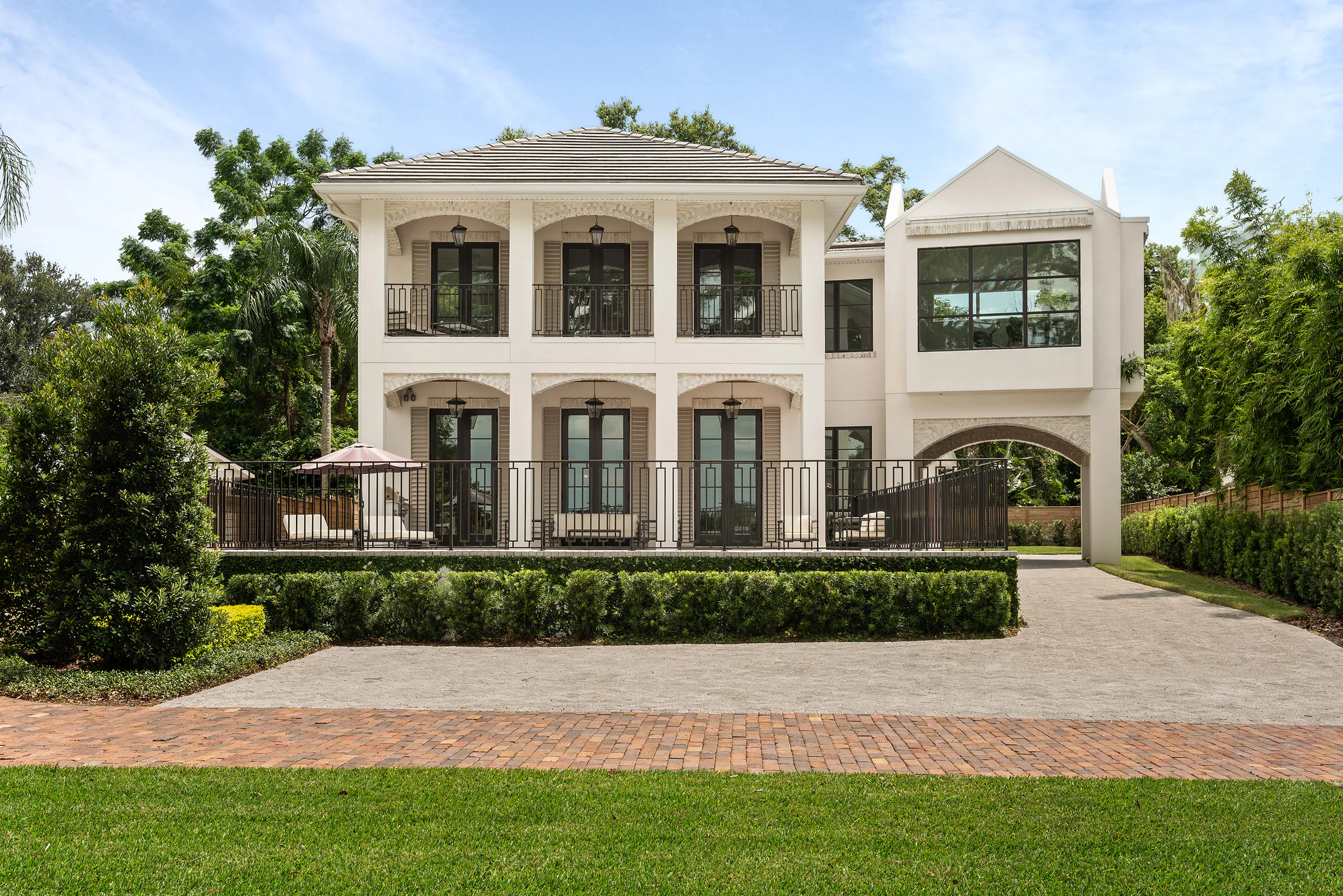 Front elevation with cream stucco, arched openings and clipped hedges.